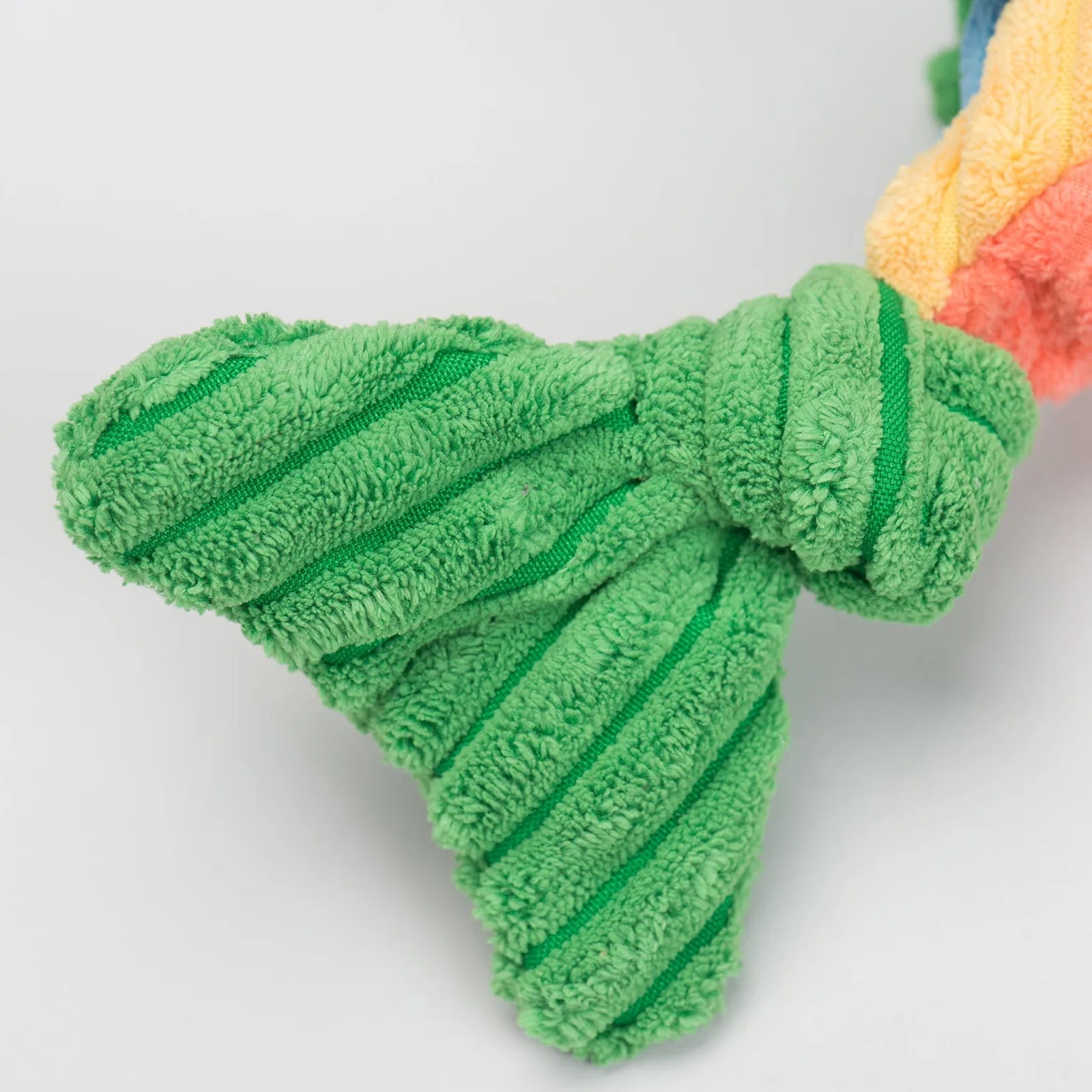 Knotted plush dog toy with a green textured tail, featuring soft material and a sturdy design for playful pups.