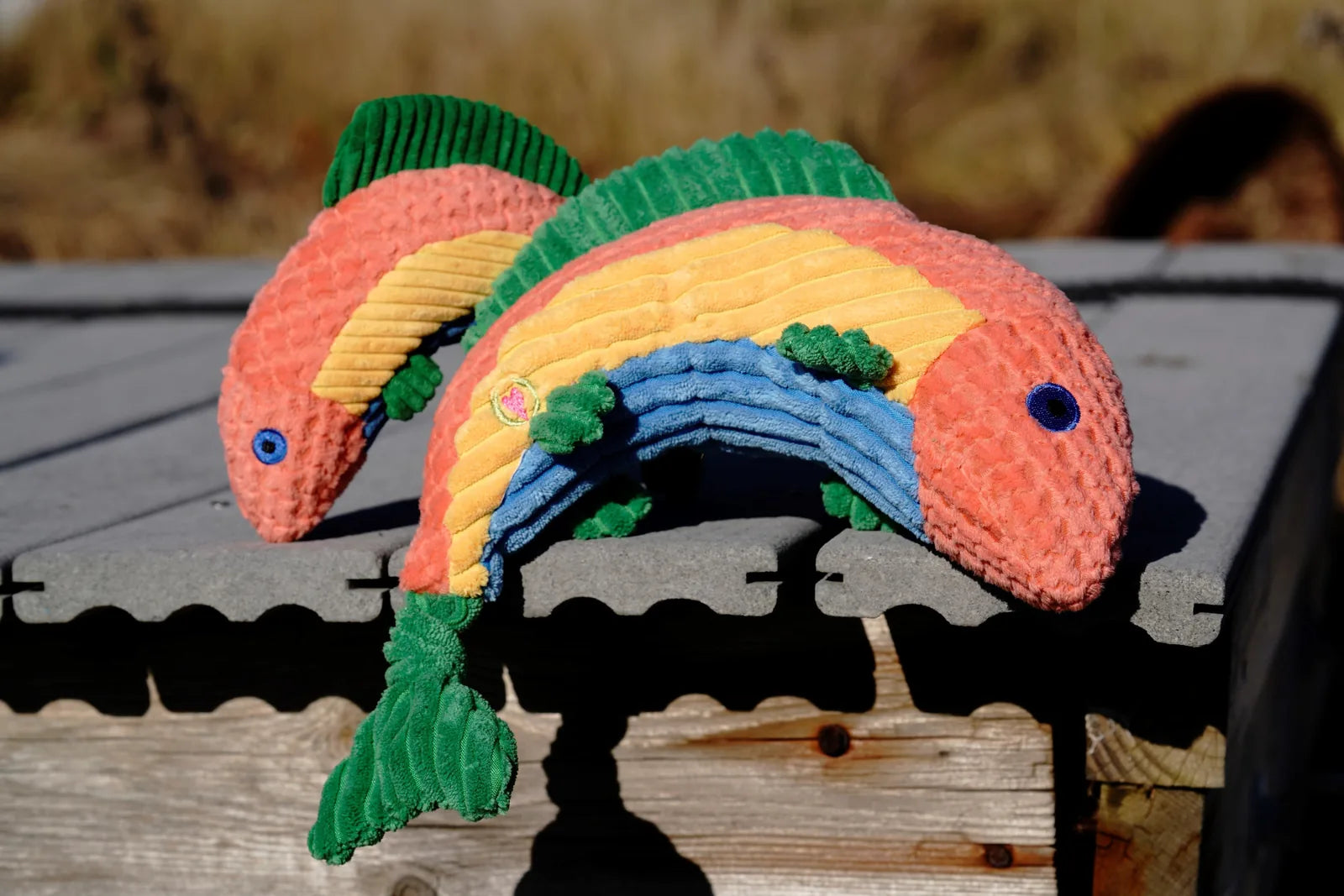 Colorful plush Rauccous Rainbow Trout Knottie® dog toy with a half-rounded shape, features blue, green, yellow, and pink p...