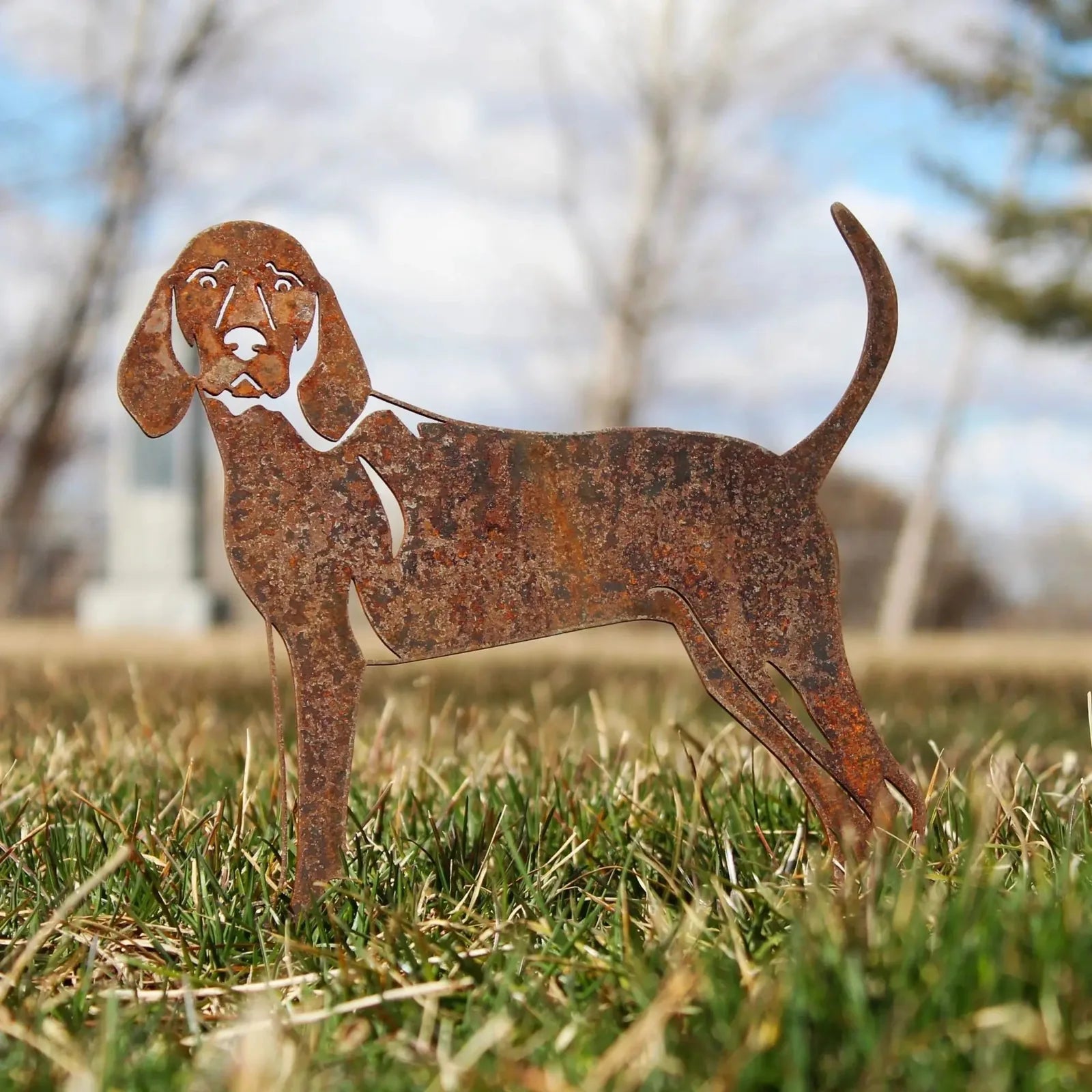Rustic Redbone Coonhound silhouette made from weathering steel, standing in grass with cloudy sky in background.