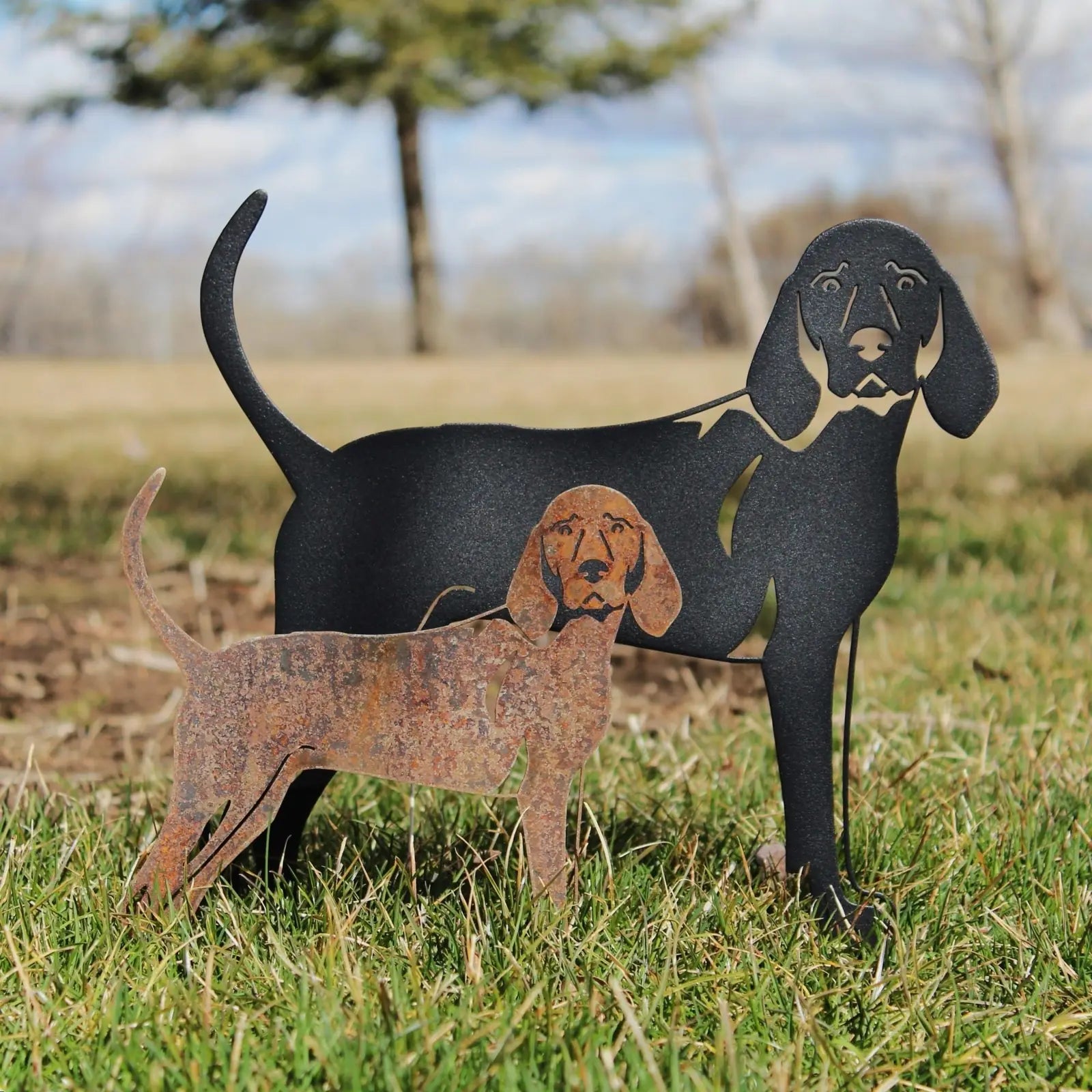 Metal silhouettes of a Redbone Coonhound in black and rust finish, set against a grassy outdoor backdrop.