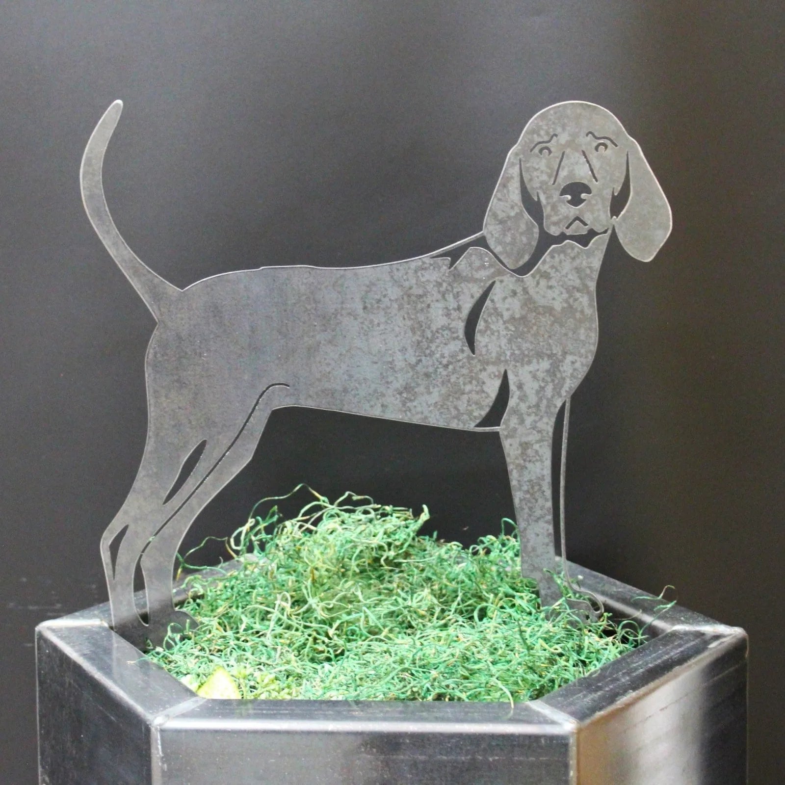 Handmade Redbone Coonhound metal silhouette in weathering steel, poised upright among green moss in a planter.