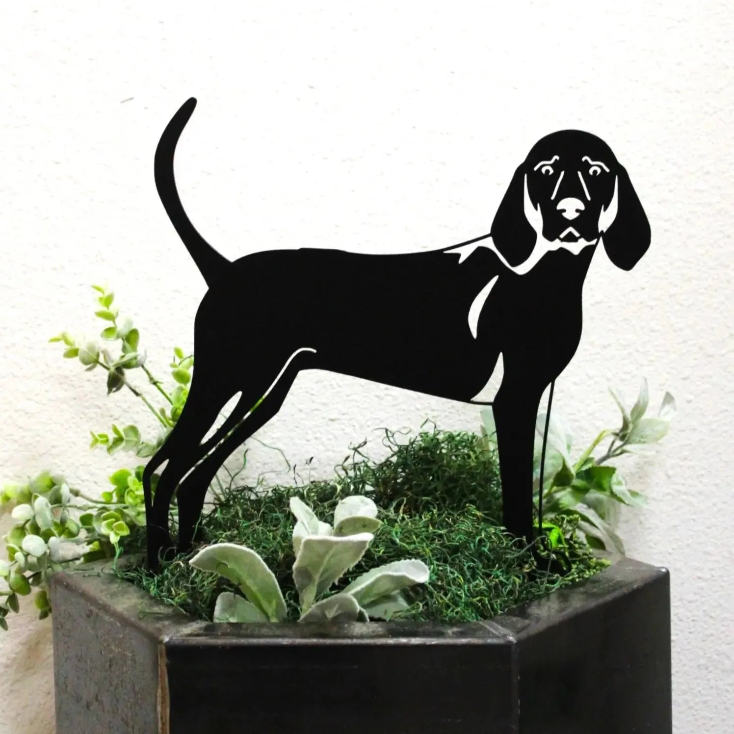 Black silhouette of a Redbone Coonhound displayed among green foliage in a planter, showcasing its elegant design.
