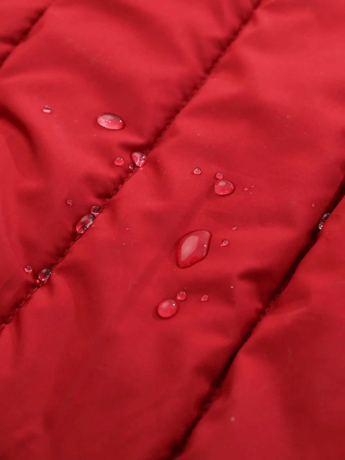 Water droplets bead on the bright red fabric of a reversible dog vest jacket, showcasing its water-repellent feature.