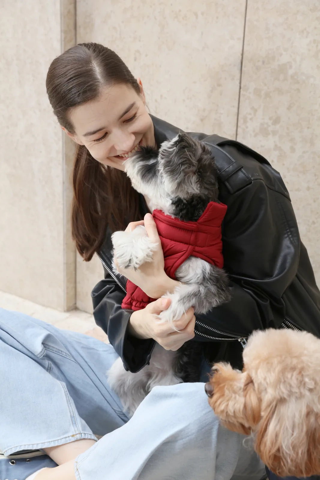 Reversible red dog vest jacket on a smiling dog, held by a young woman in a stylish black leather jacket.