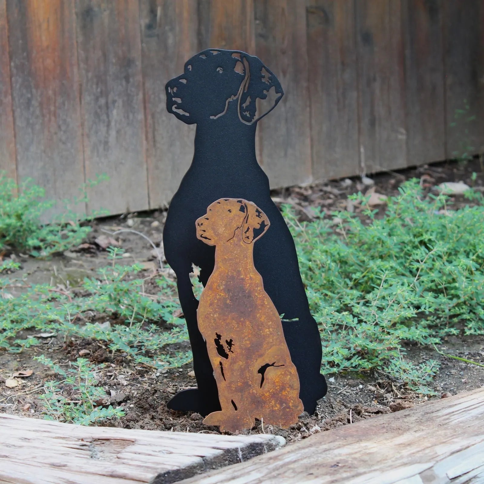 Rhodesian Ridgeback metal silhouette in black and rust-colored Corten steel, surrounded by greenery.