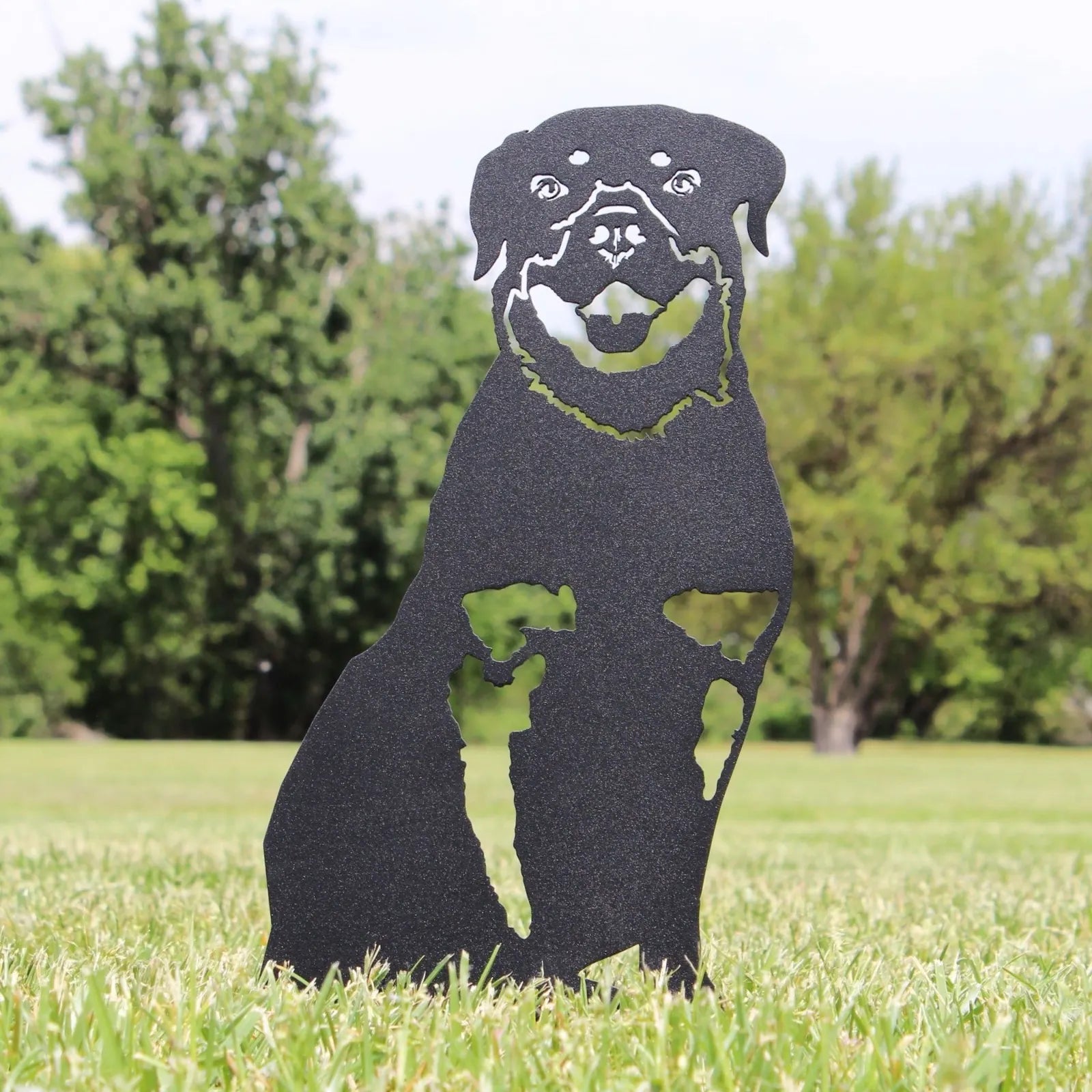 Black metal silhouette of a Rottweiler, designed for outdoor decor, standing on grass with trees in the background.
