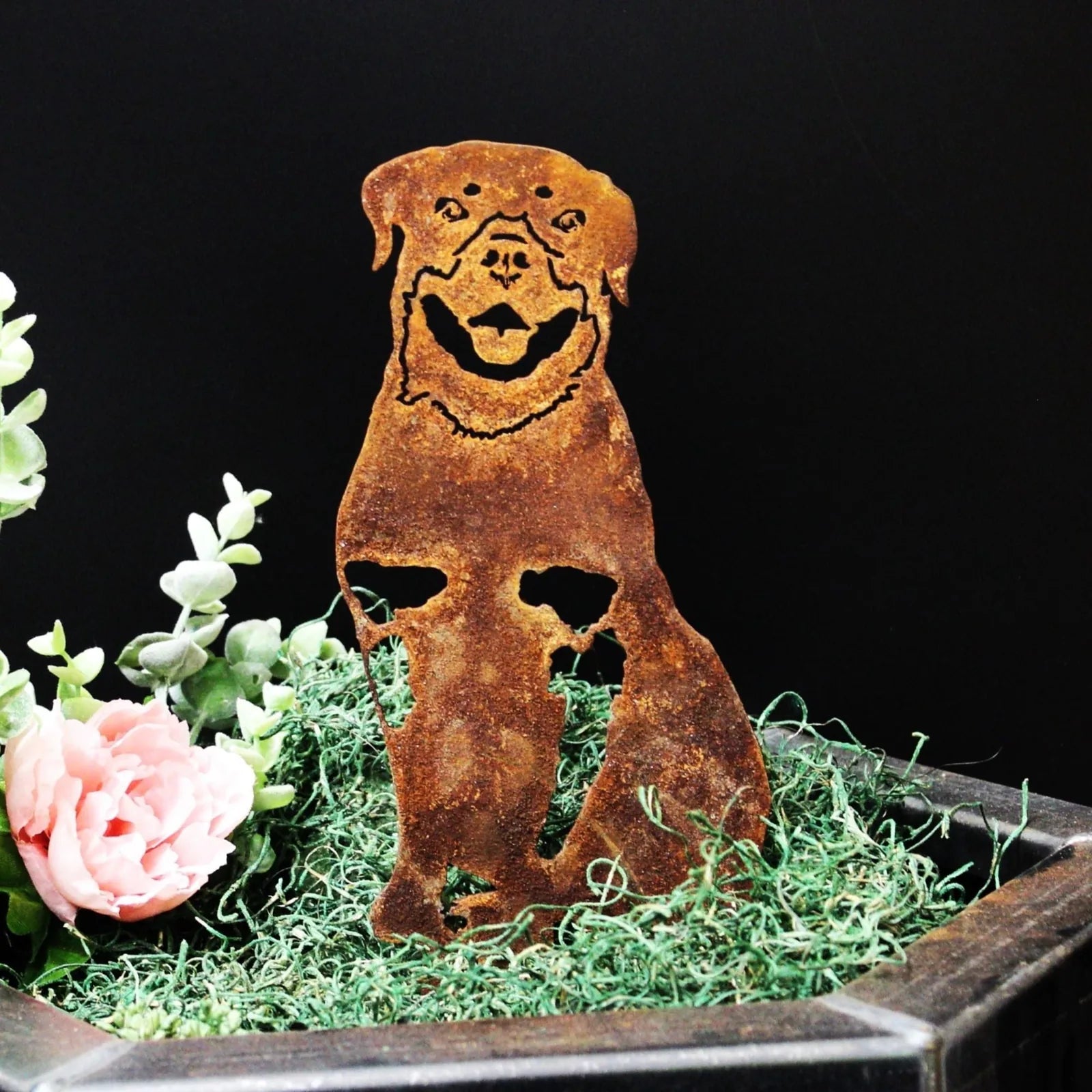 Rust-colored Rottweiler metal silhouette on green moss, ideal for outdoor dog decor.