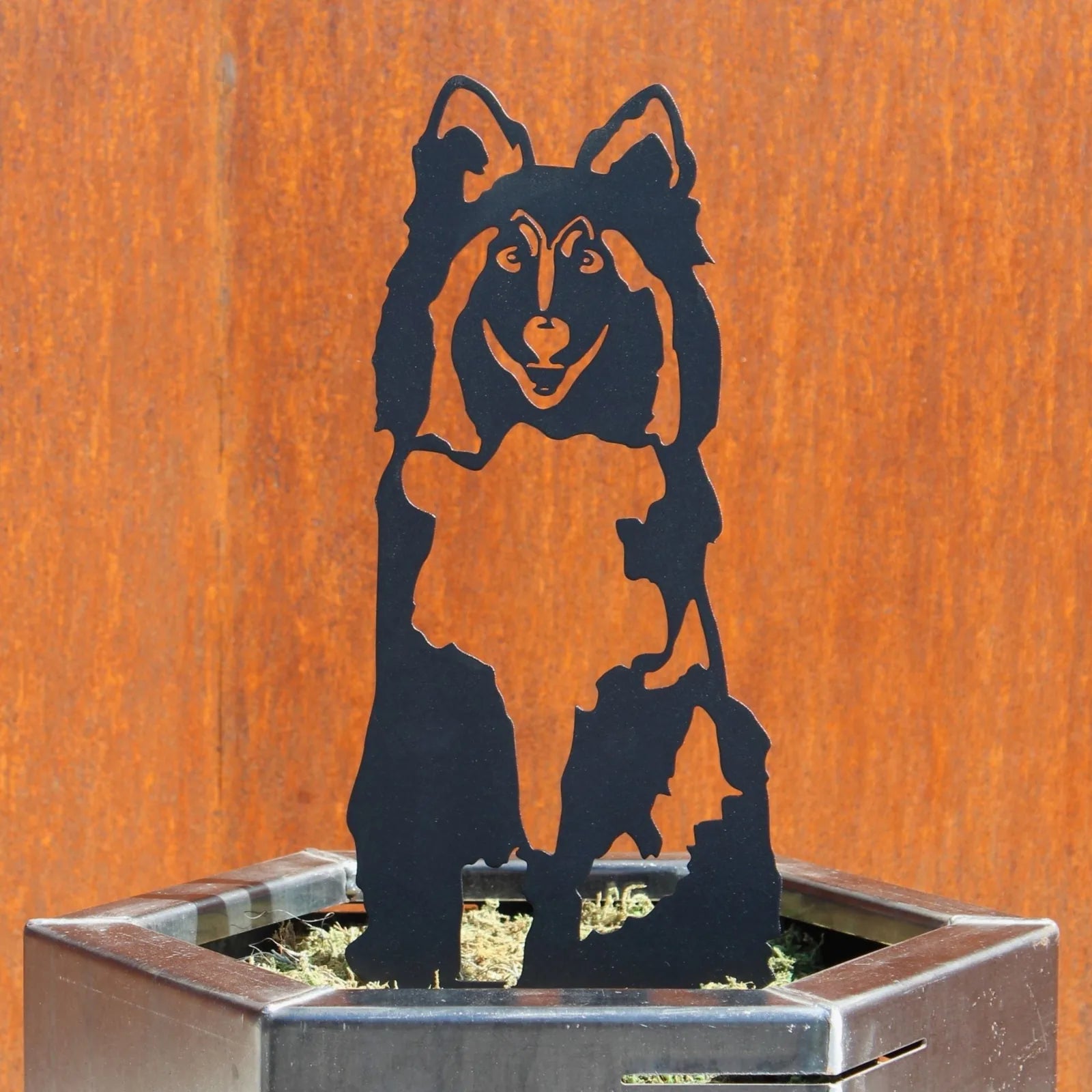 Black metal silhouette of a Rough Collie, set against a rust-colored backdrop in a planter. Ideal dog decor for outdoor sp...