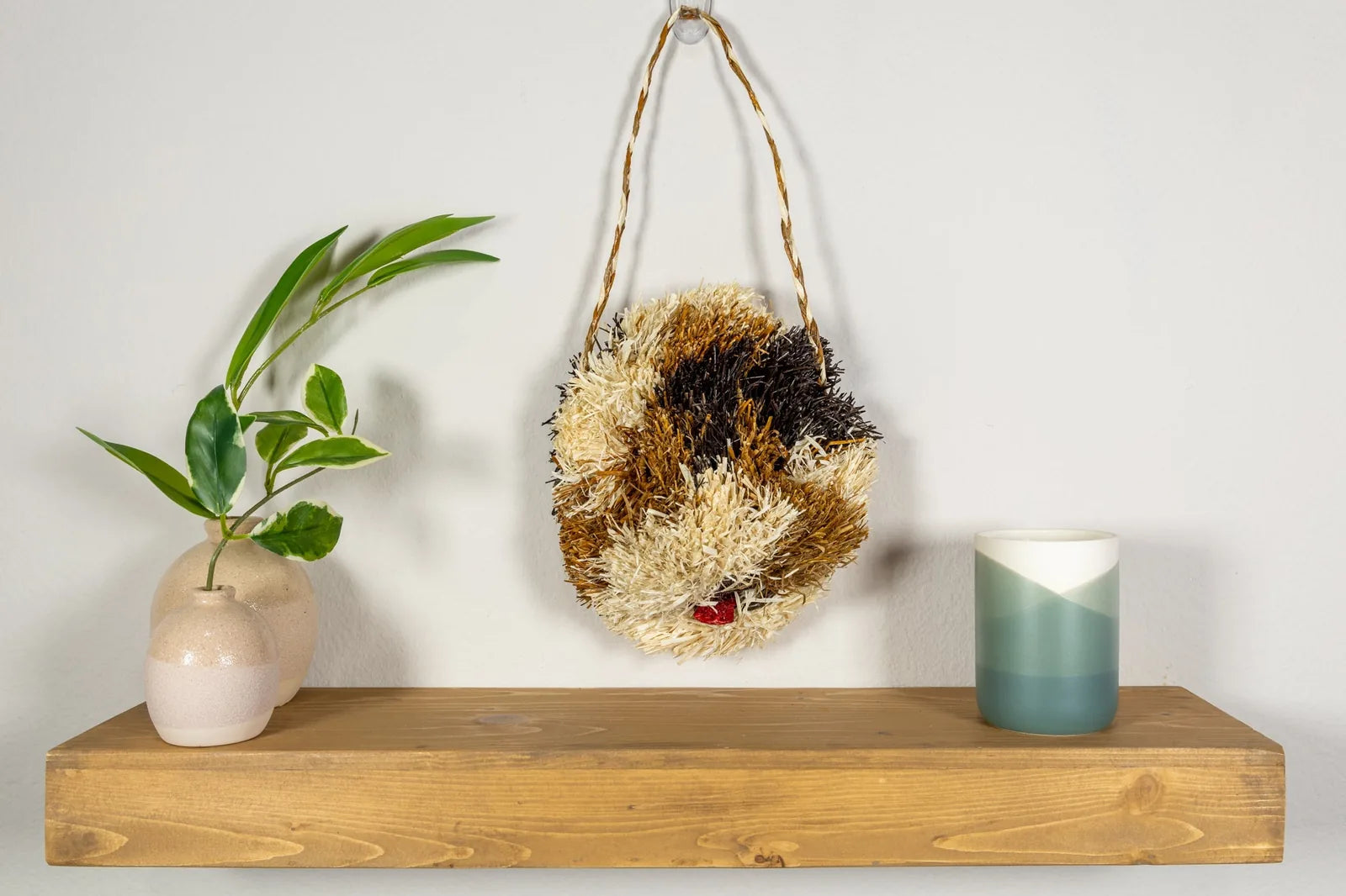Handwoven Saint Bernard dog mask in earthy tones, representing Indigenous artistry, hung on a wooden shelf with decor.