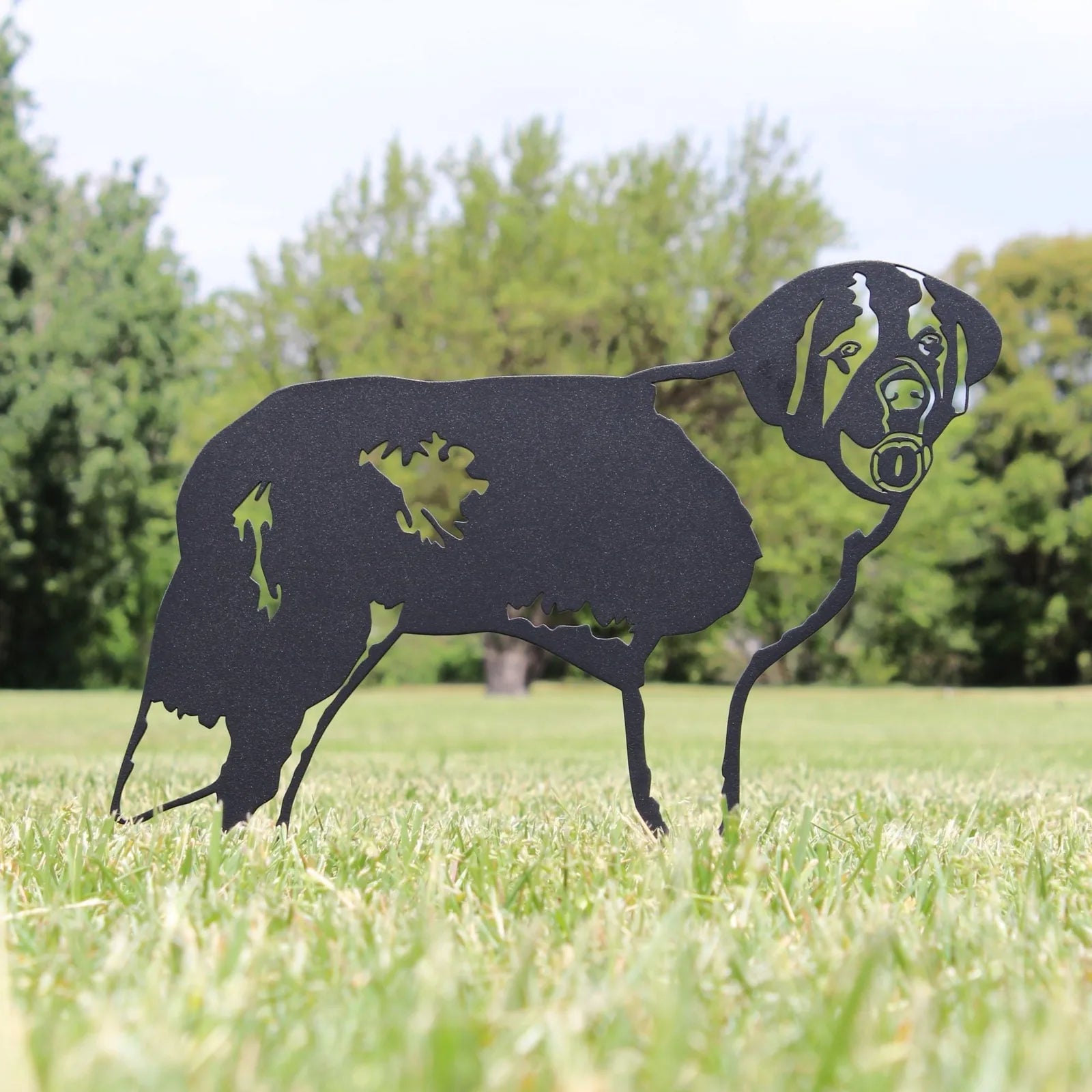 Black metal silhouette of a Saint Bernard dog stands on a grassy field, highlighting its crafted design for outdoor decor.
