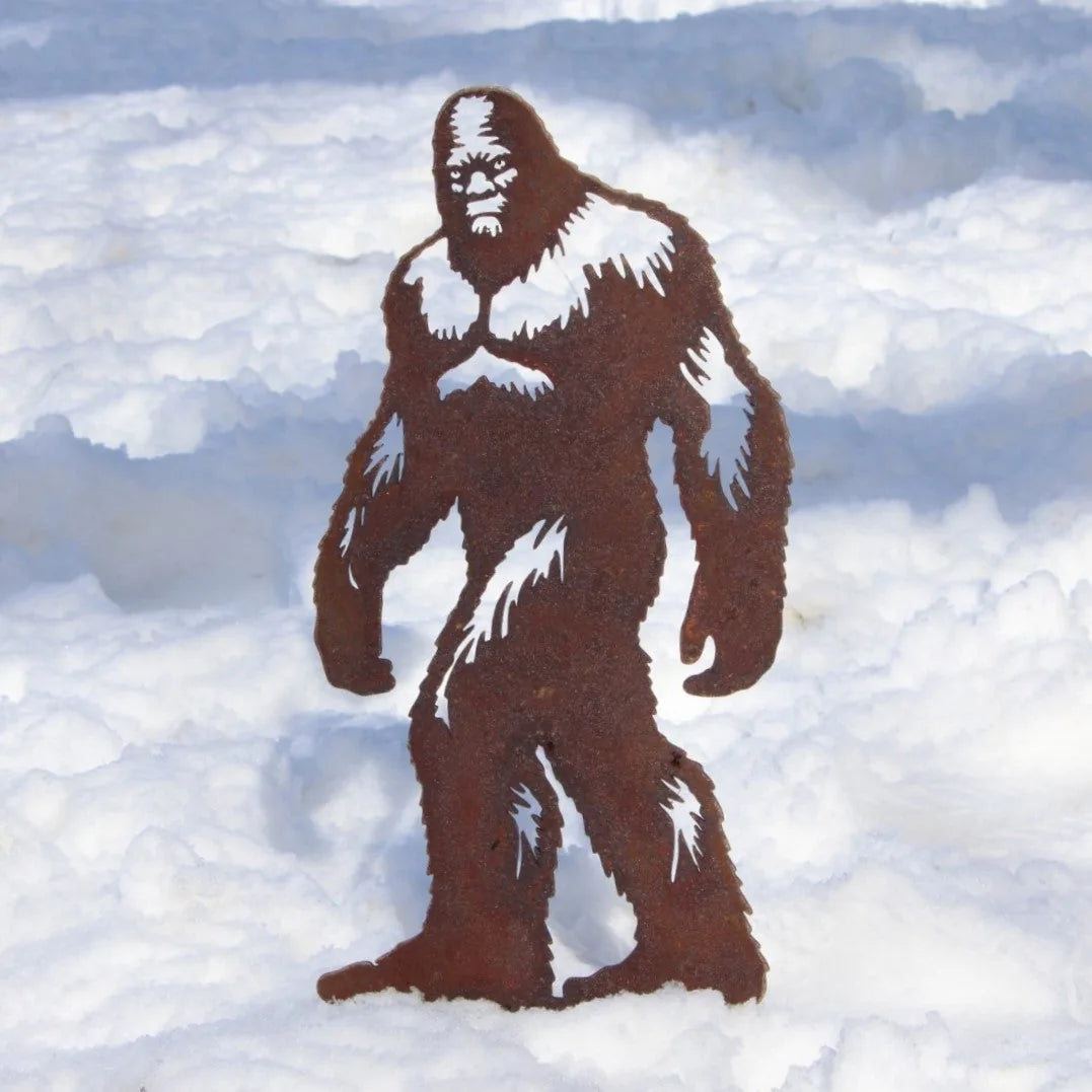 Sasquatch metal silhouette in rusty Corten steel, standing amidst white snow, ideal for outdoor decor.