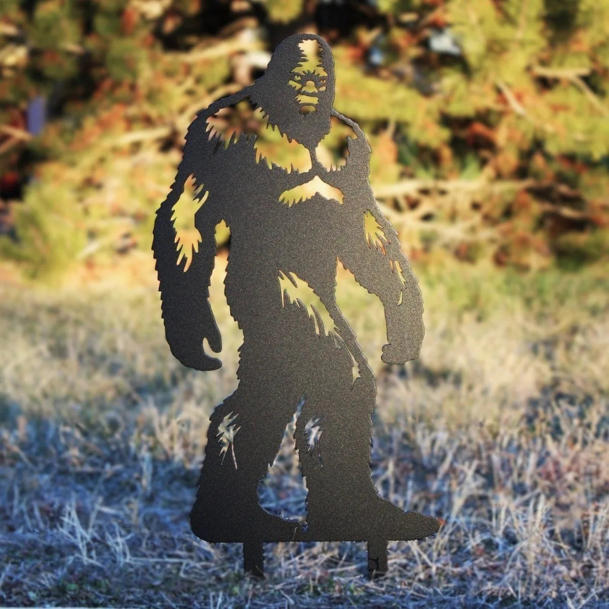 Sasquatch metal silhouette in matte black, standing on grass with a blurred outdoor background. Handmade from sturdy steel.