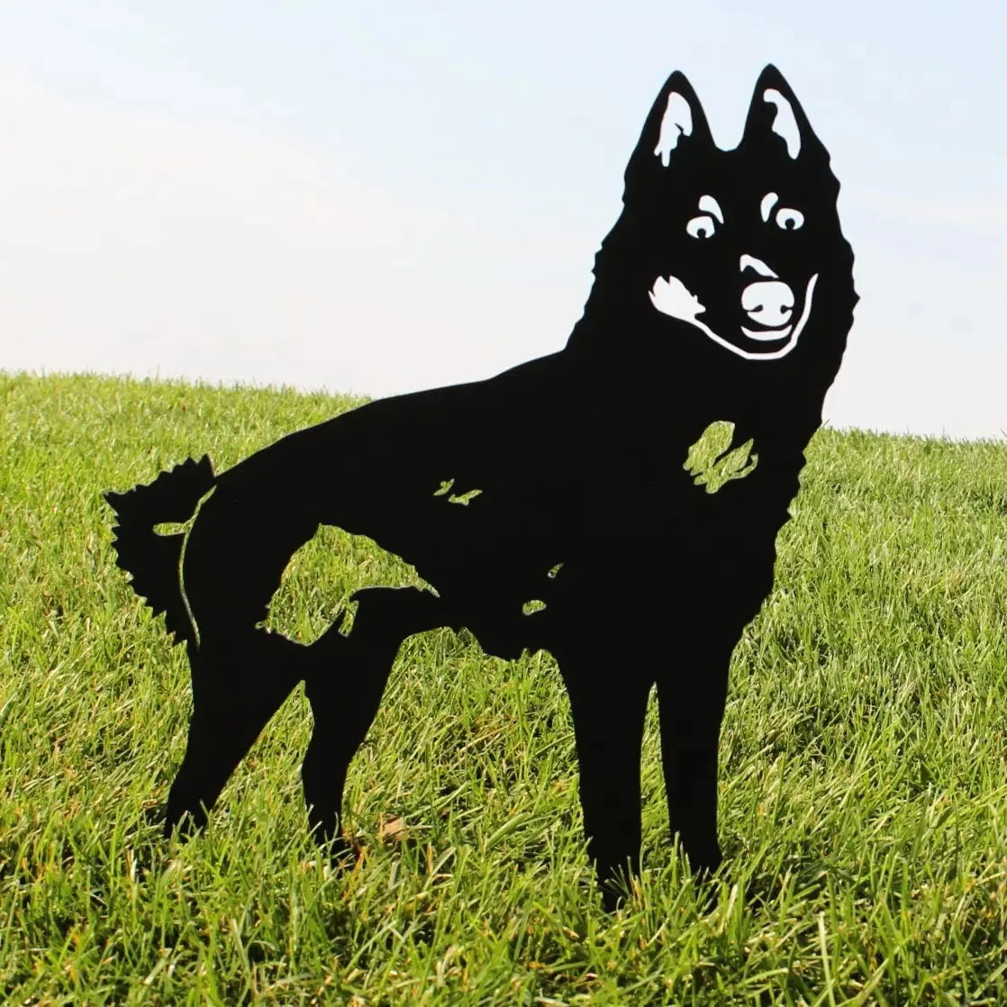 Black metal silhouette of a Schipperke dog standing in lush green grass against a clear sky background.