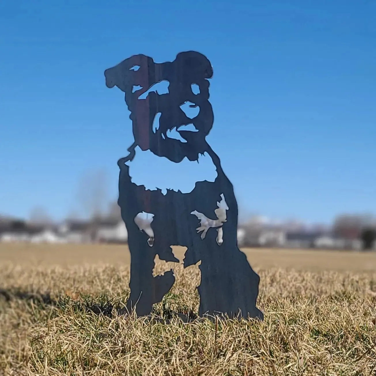 Schnauzer silhouette crafted from Corten steel, standing in a grassy field against a blue sky.