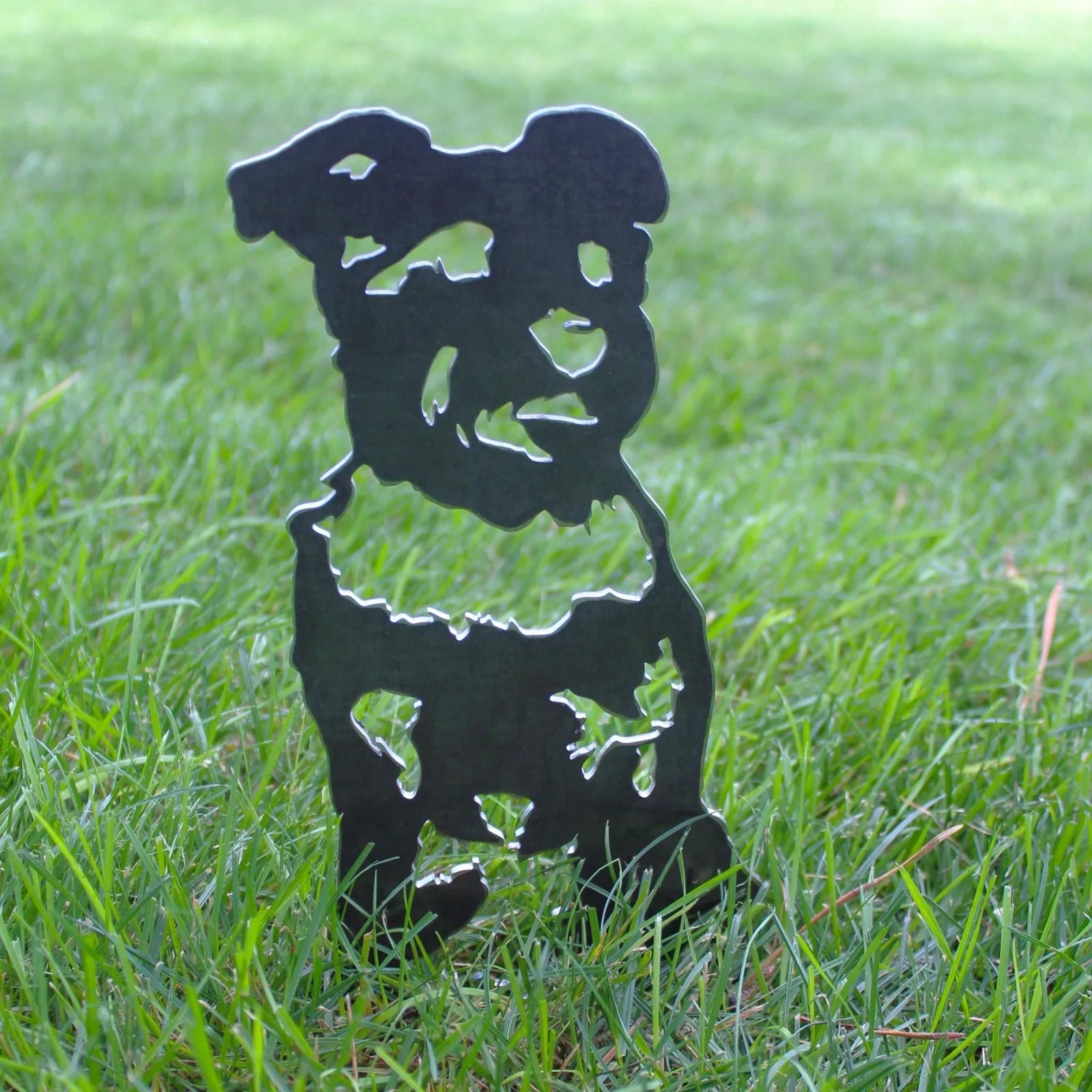 Black Schnauzer metal silhouette art standing in green grass, showcasing intricate cutout design for outdoor decor.