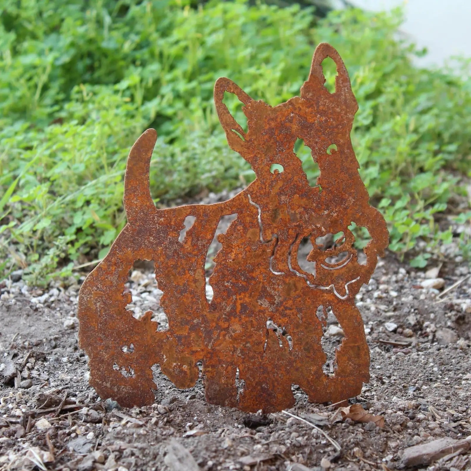 Rusty Scottish Terrier metal silhouette garden art against greenery, showcasing intricate cut-out details and a playful de...