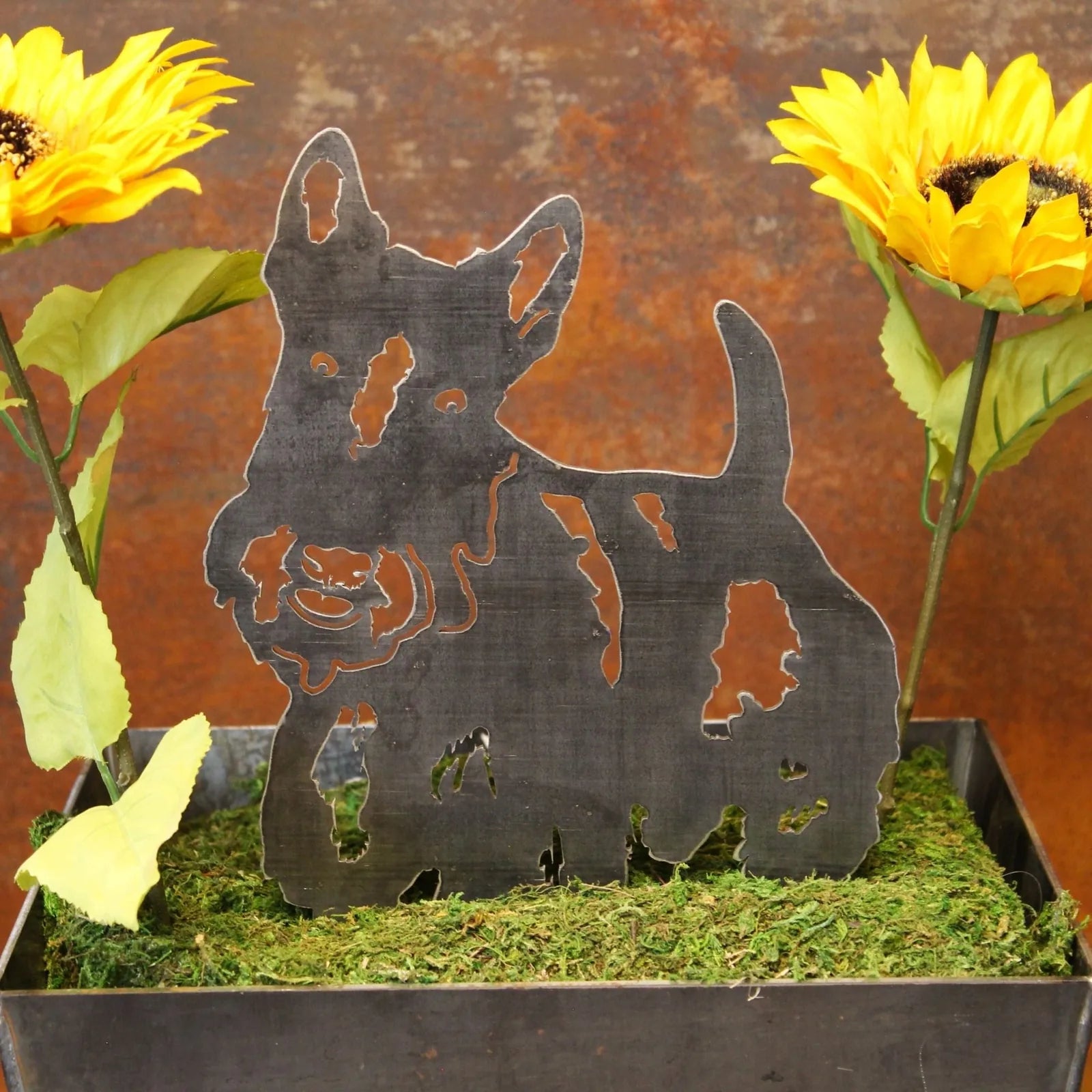 Scottish Terrier metal silhouette in black, surrounded by faux sunflowers and greenery in a planter.