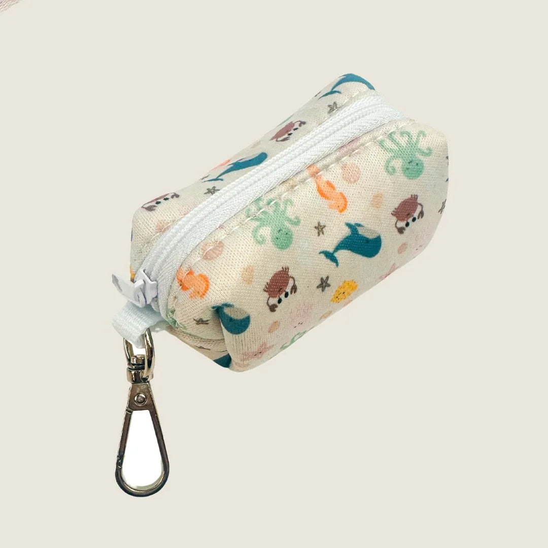 Lightweight neoprene waste bag in off-white with playful marine-themed patterns, complete with a metal swivel hook.