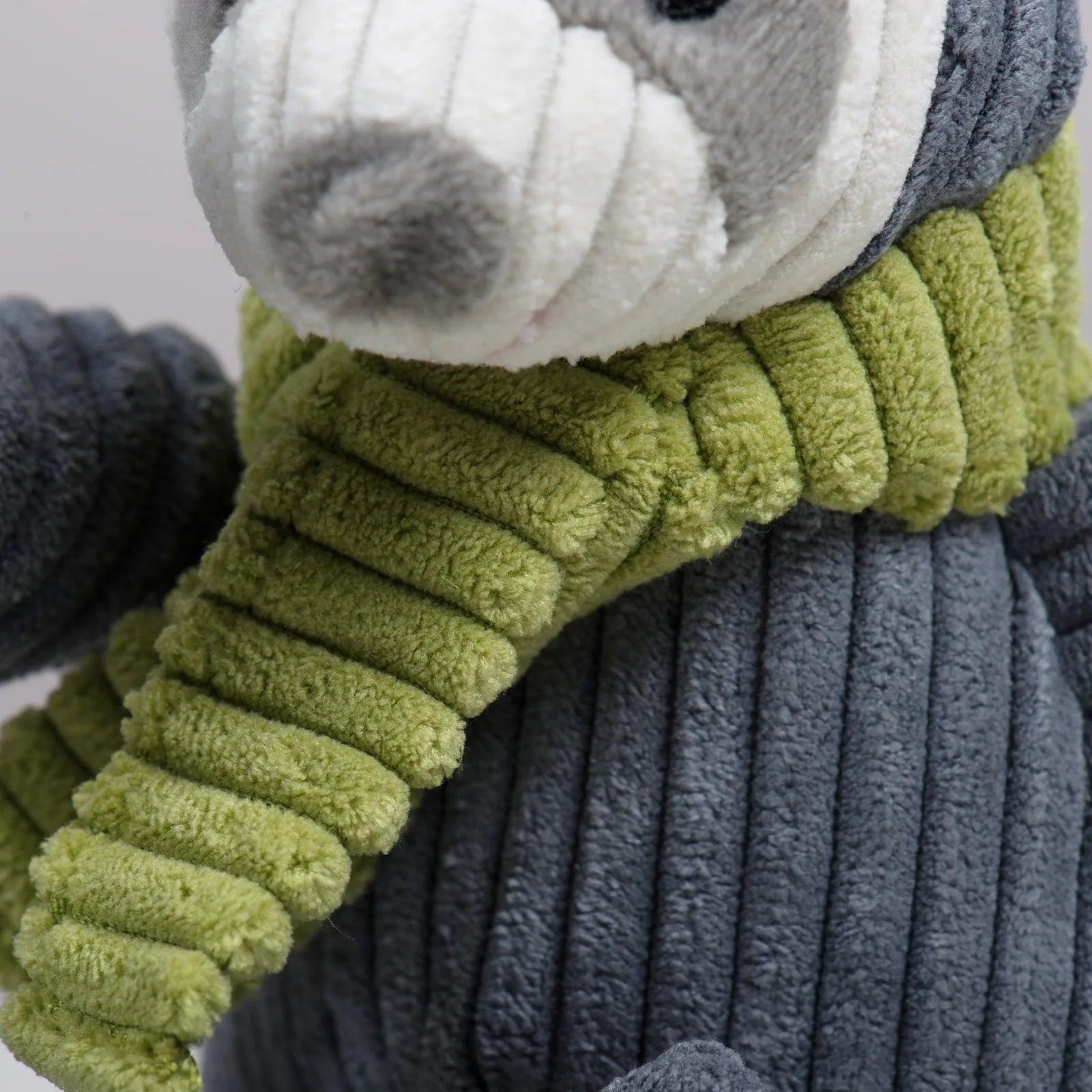 Close-up of Seb Sloth Knottie® plush dog toy, featuring a grey body and a green ribbed scarf. Soft, textured fabric.
