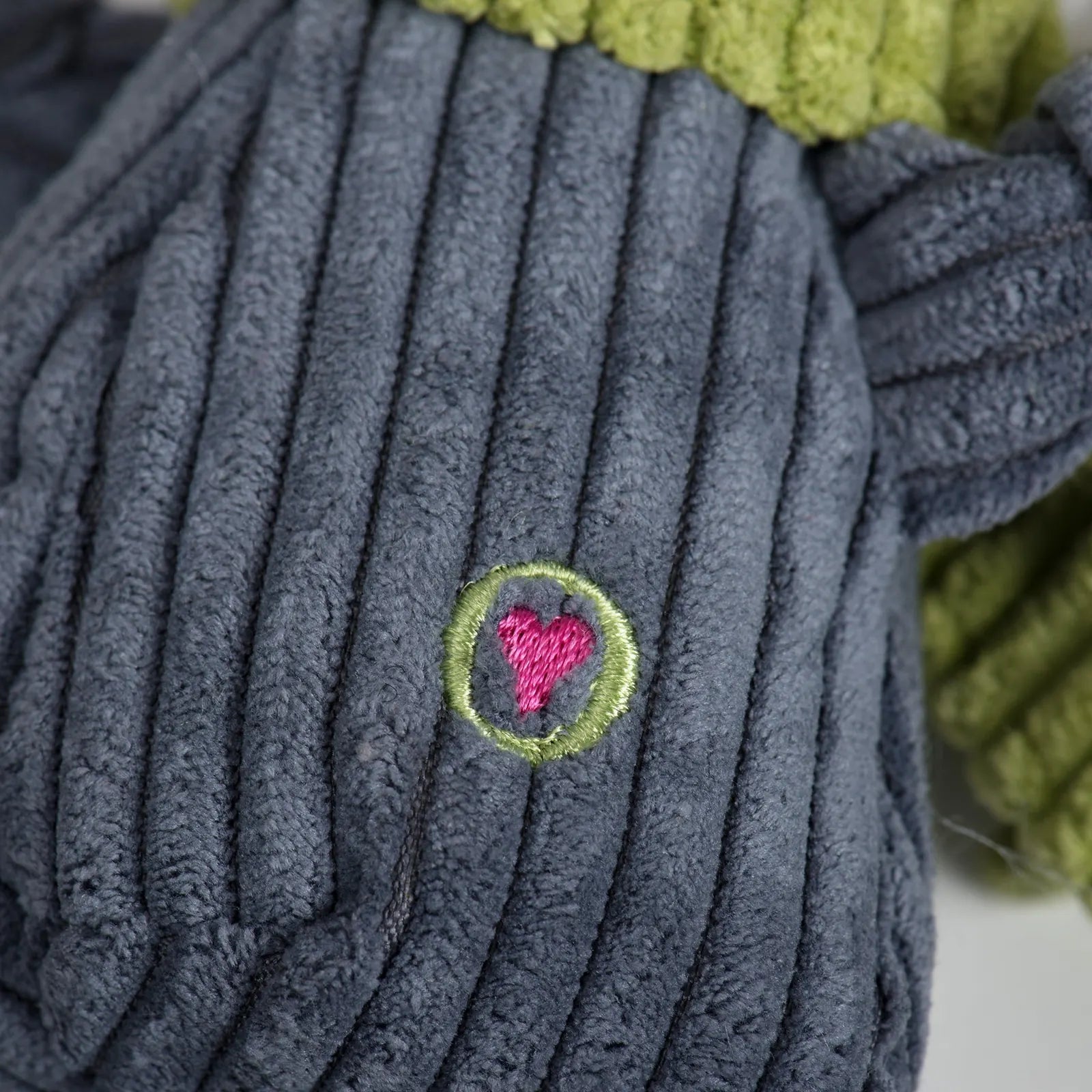 Close-up of Seb Sloth Knottie® dog toy, featuring a soft gray corduroy texture with a green scarf and a pink heart embroid...