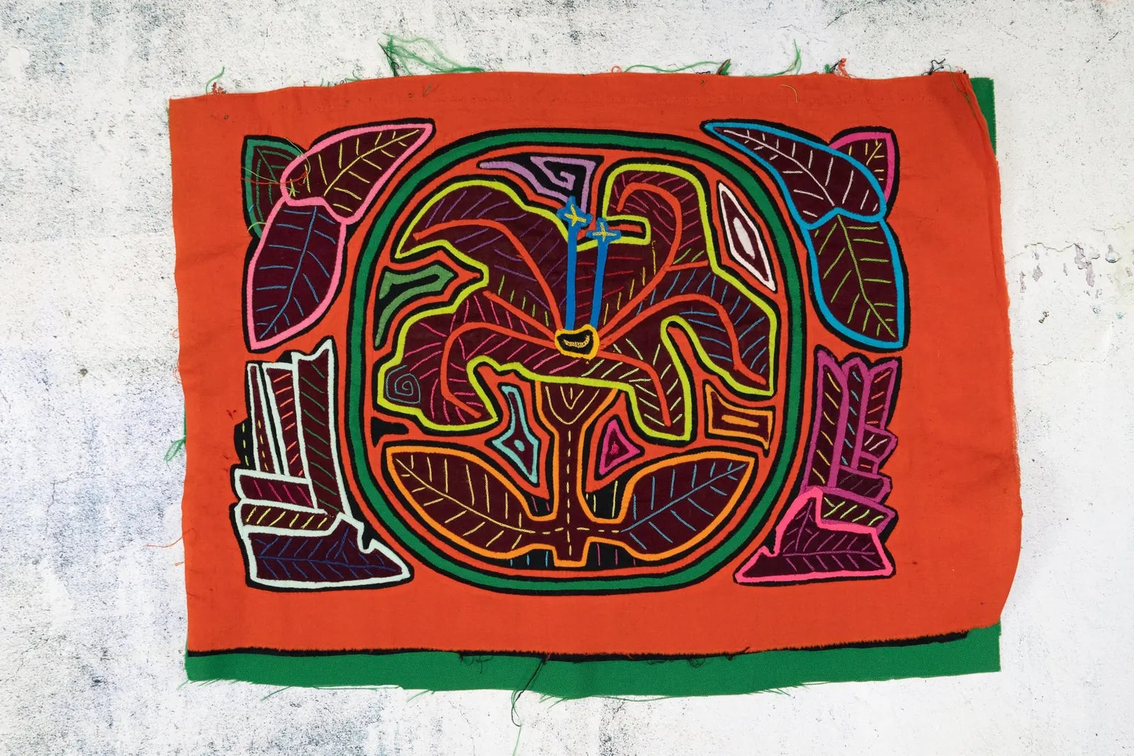 Colorful hand-stitched tapestry featuring a shaggy puppy with flowers, showcasing vibrant patterns on an orange background.
