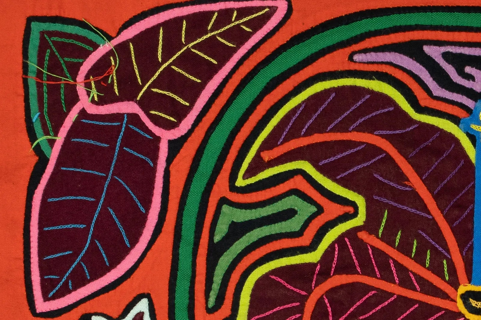 Colorful hand-stitched leaves with intricate patterns on vibrant orange fabric, showcasing traditional Panama Mola art.