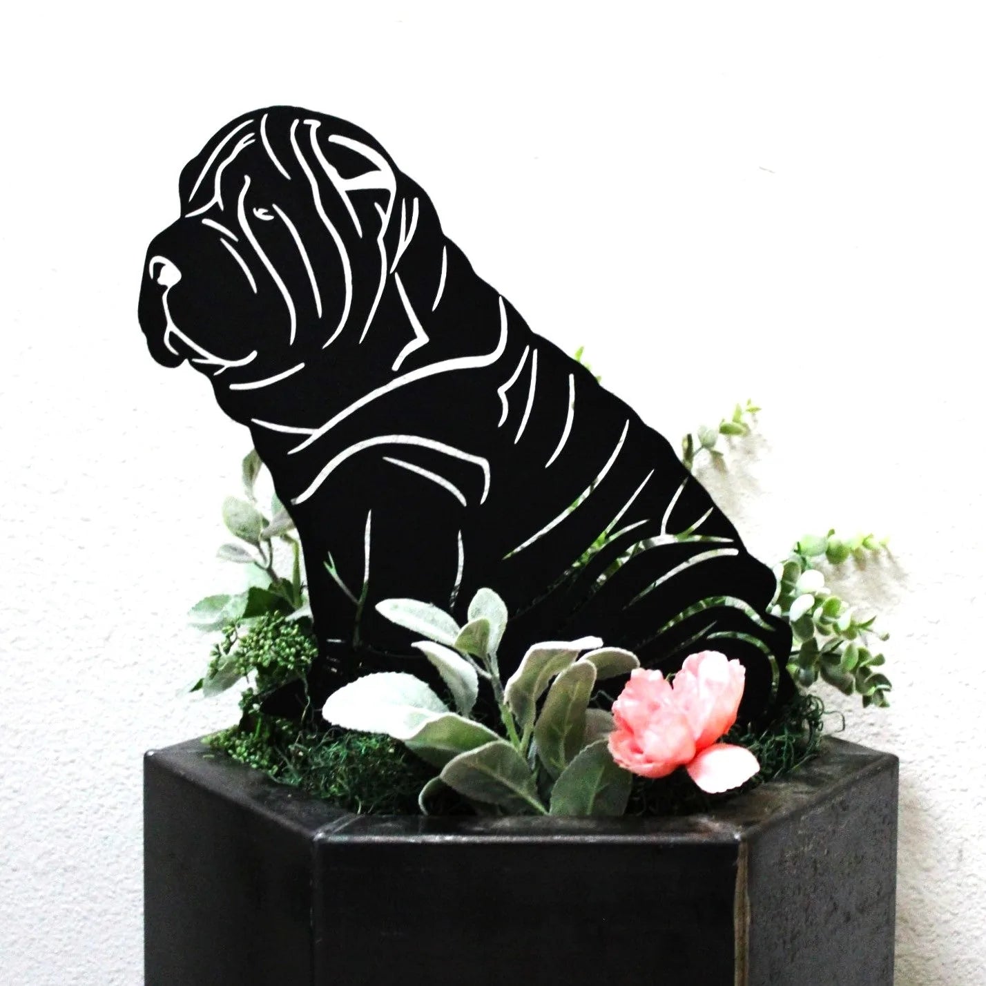 Black metal silhouette of a sitting Shar Pei dog surrounded by greenery and a pink flower, ideal for outdoor decor.