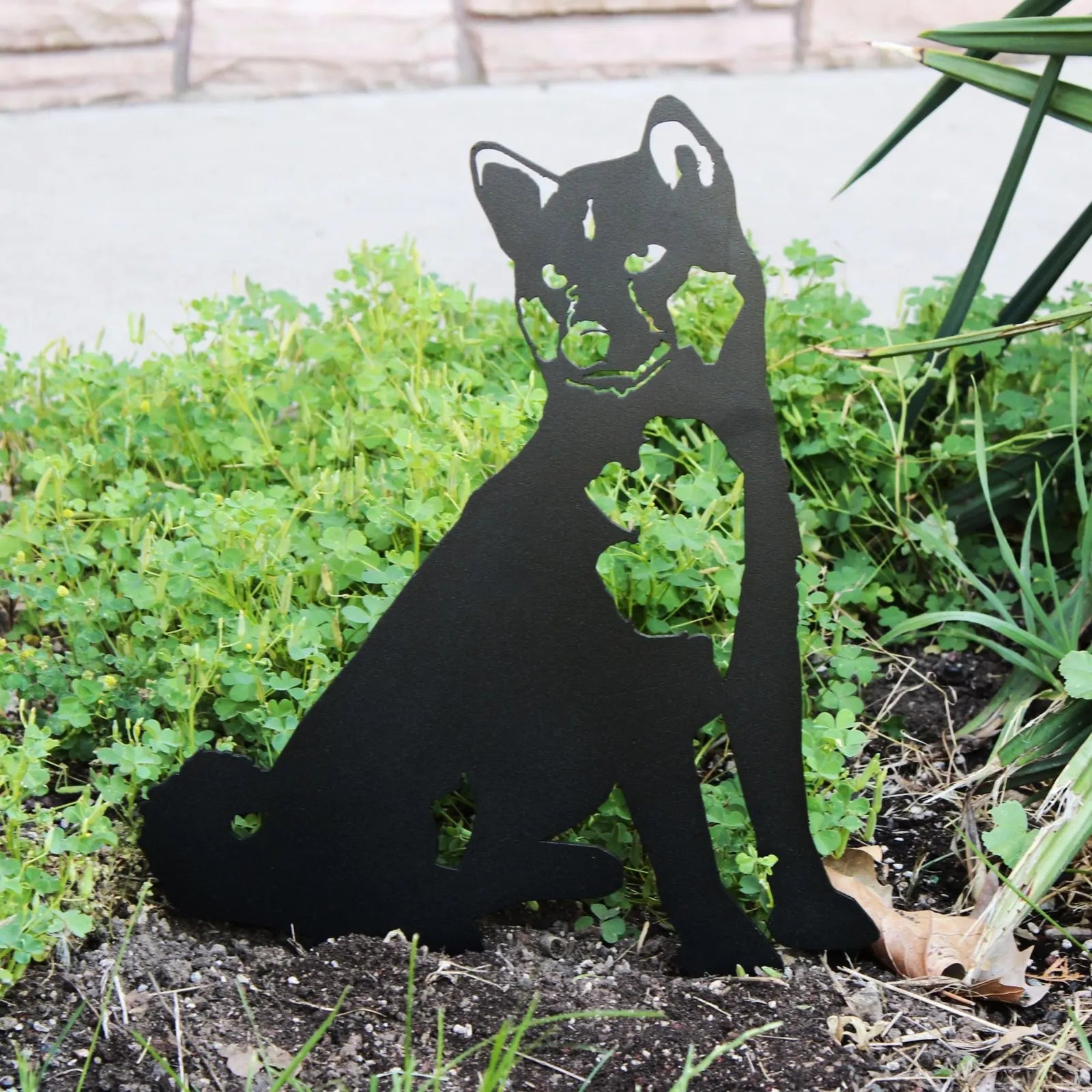 Black Shiba Inu metal silhouette art displayed among greenery, showcasing a rustic charm for outdoor decor.