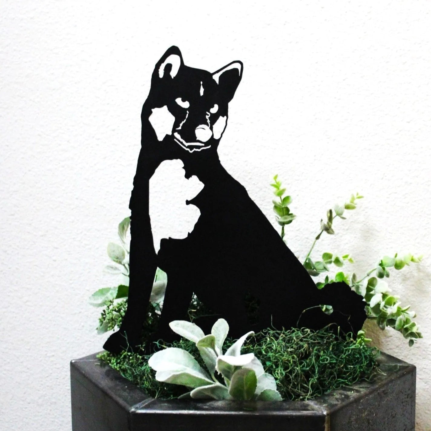 Black Shiba Inu metal silhouette art in a planter with green foliage, adding rustic charm to outdoor decor.