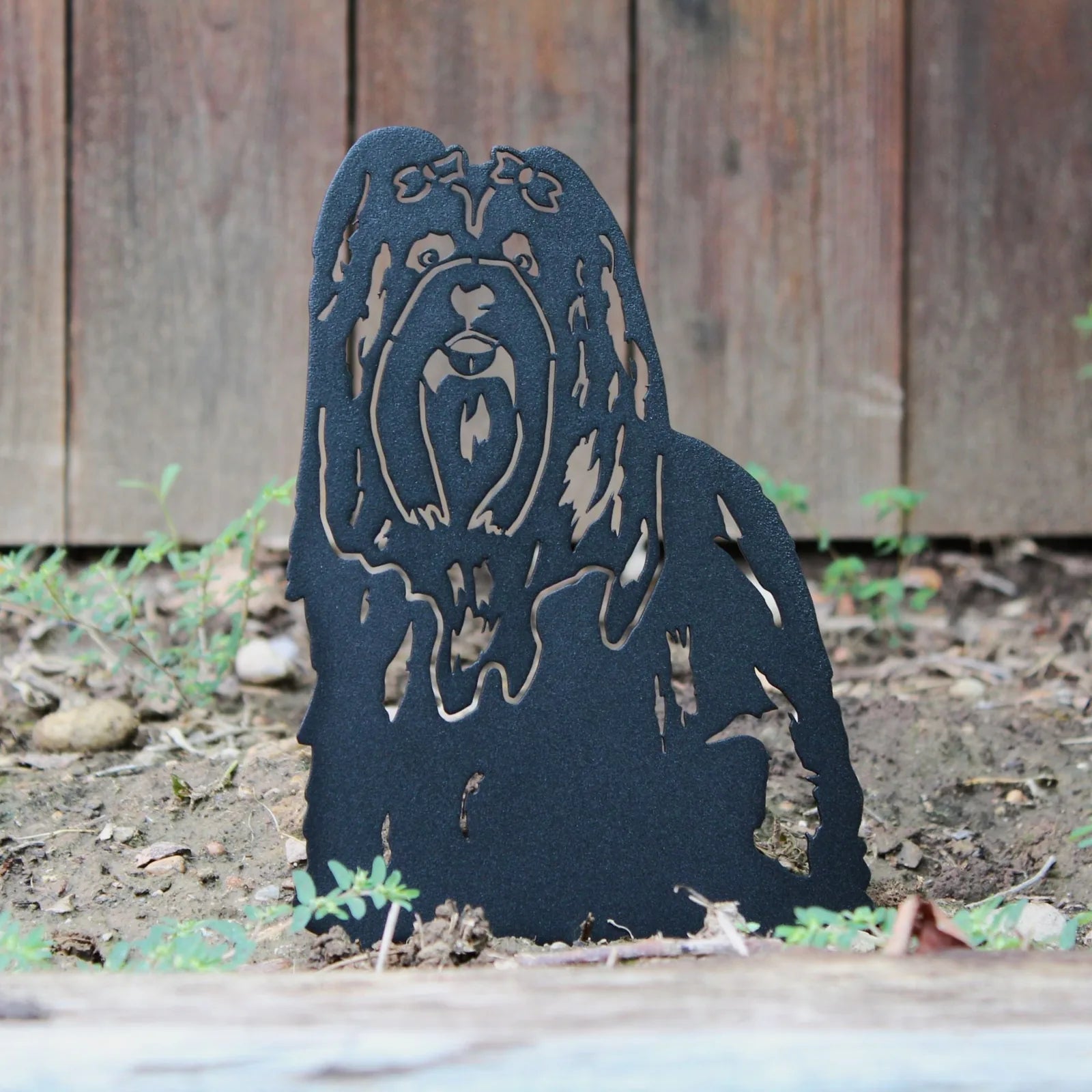 Black metal silhouette of a Shih Tzu dog, showcasing intricate cutout details against a natural garden setting.