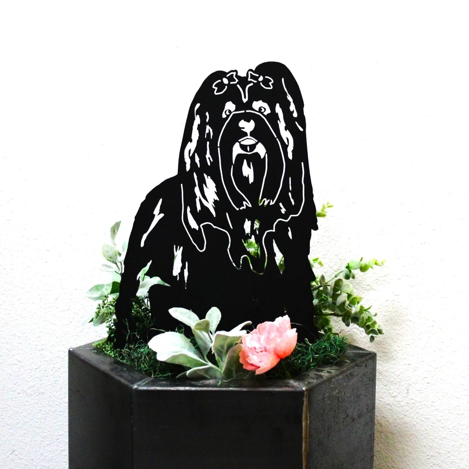 Black metal silhouette of a Shih Tzu dog, displayed with greenery and pink flowers in a decorative planter.