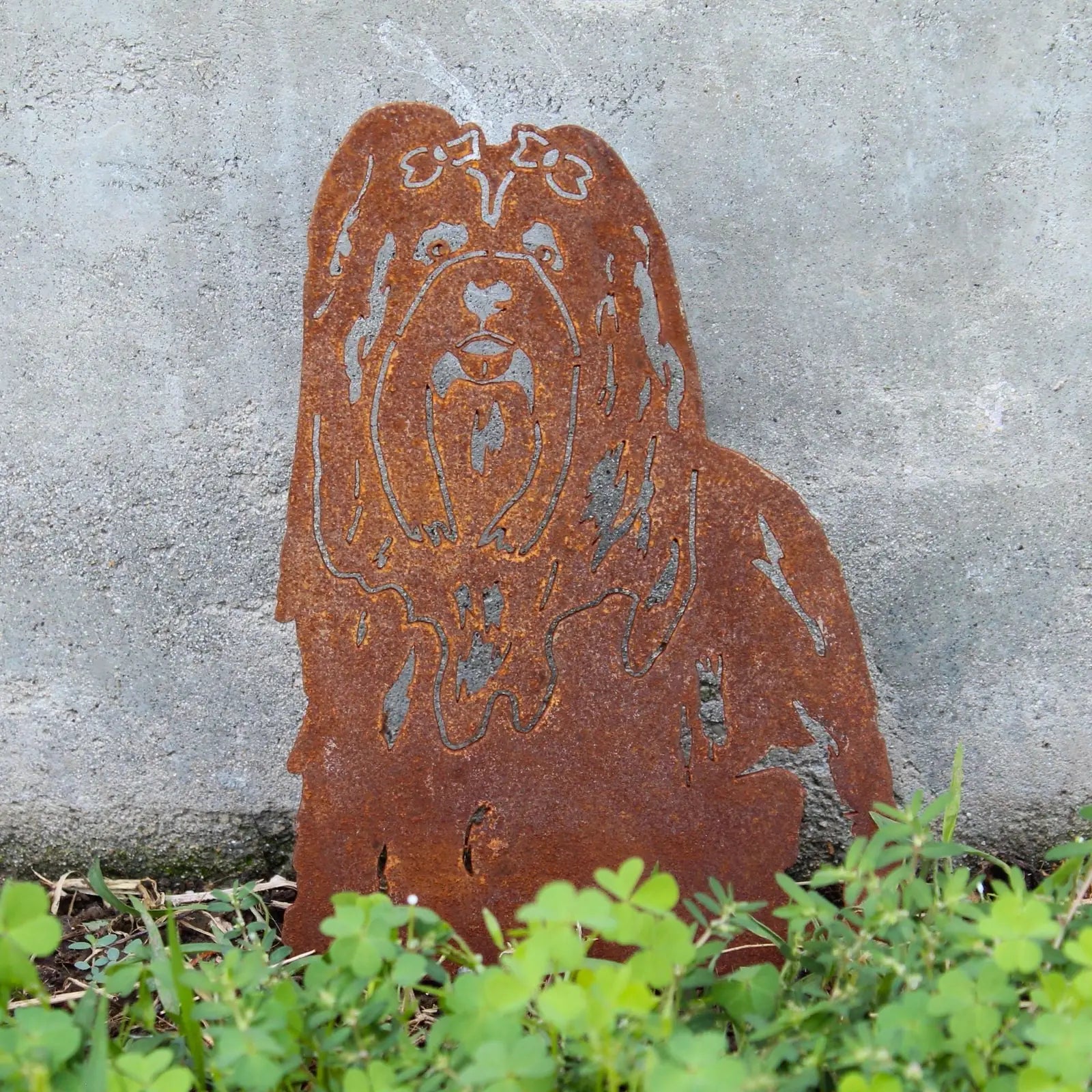 Rusty metal silhouette of a Shih Tzu dog, surrounded by greenery, showcasing a unique weathered texture.