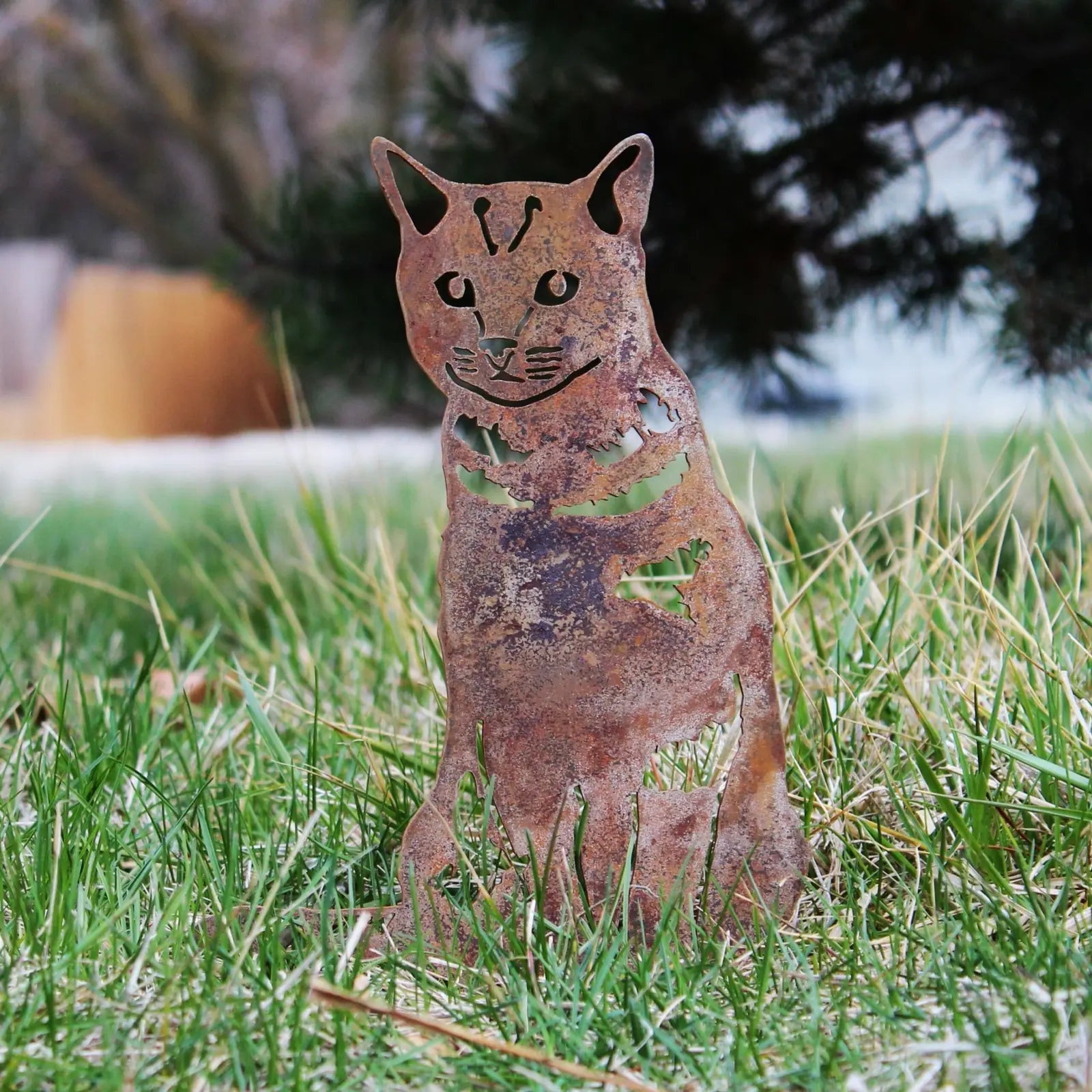 Rustic metal silhouette of a shorthair tabby cat in weathered Corten steel, set against grassy outdoor decor.
