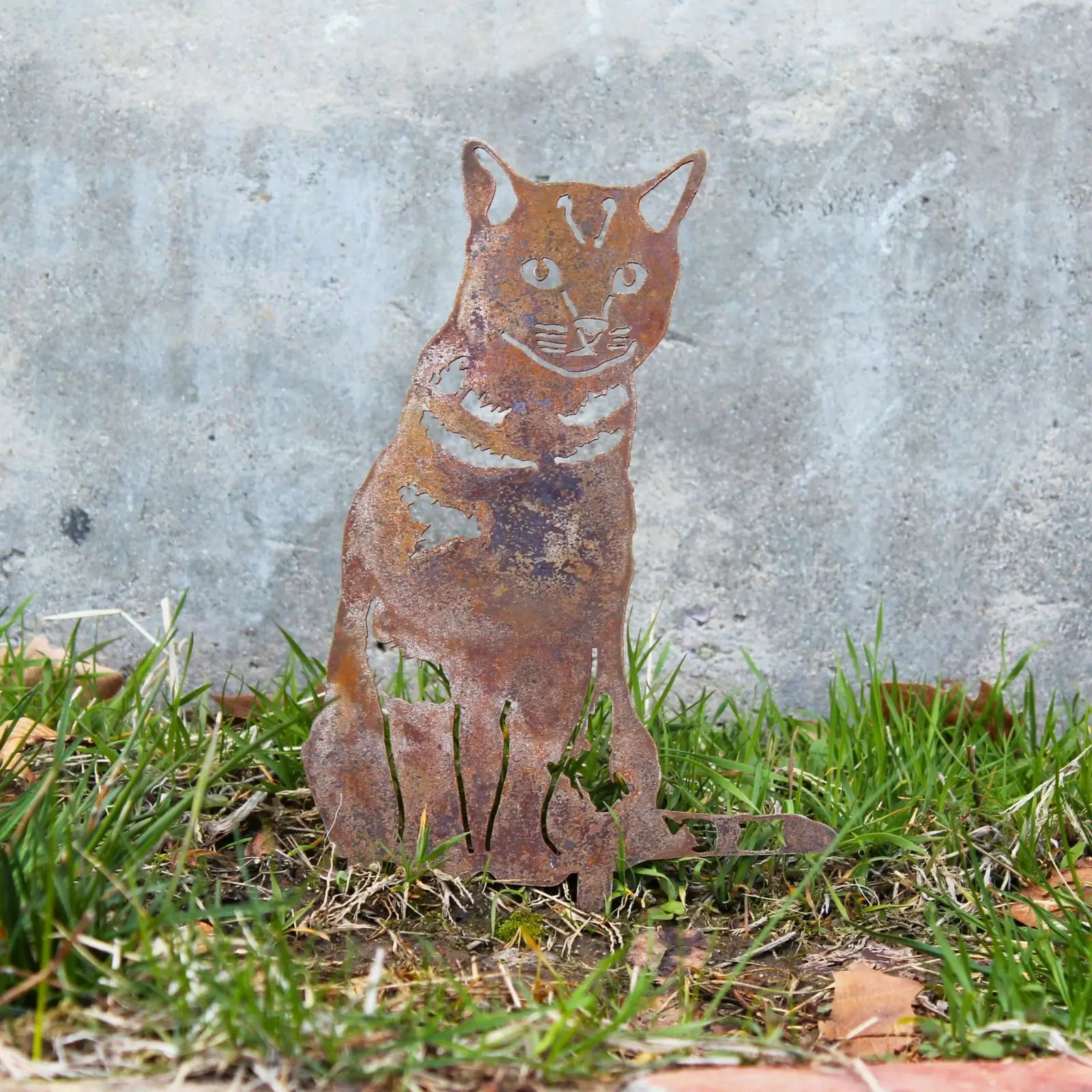 Rusty Corten steel silhouette of a shorthair tabby cat sitting in green grass, showcasing a rustic outdoor art design.