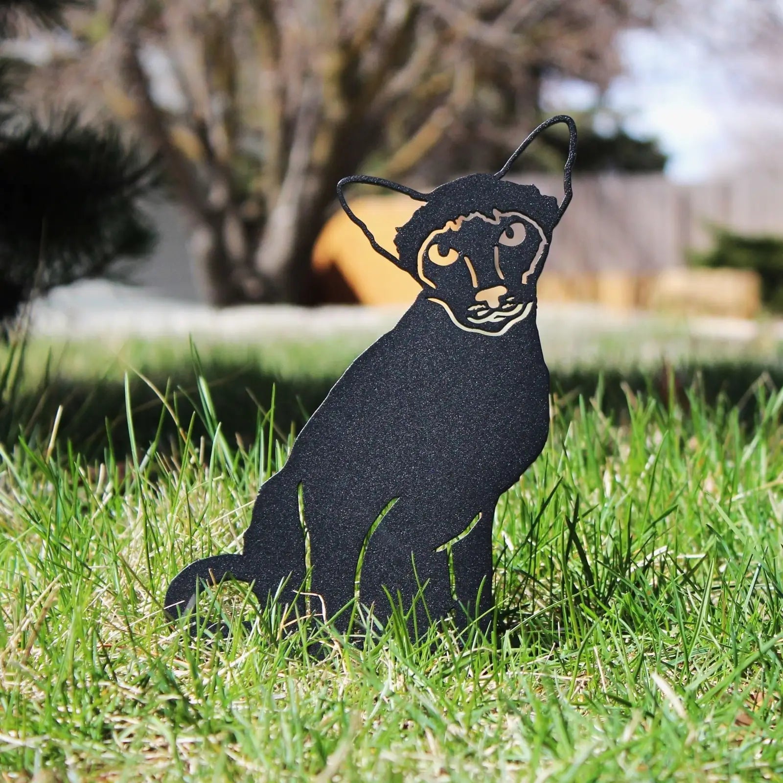 Black metal Siamese cat silhouette with detailed features, set among green grass in a garden environment.