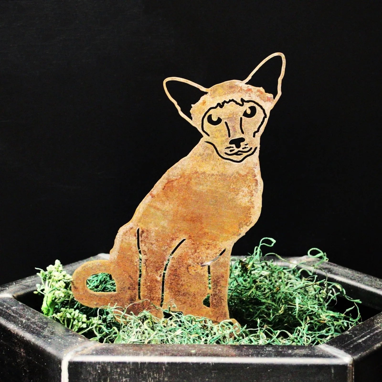 Rust-colored Siamese cat silhouette made from Corten steel, perched in decorative moss within a planter.