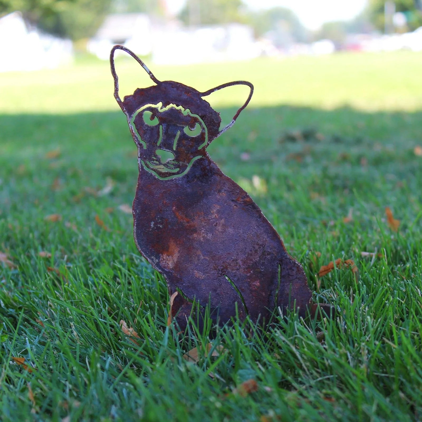 Handmade Siamese cat silhouette in weathered Corten steel, positioned in green grass, ideal for garden decoration.