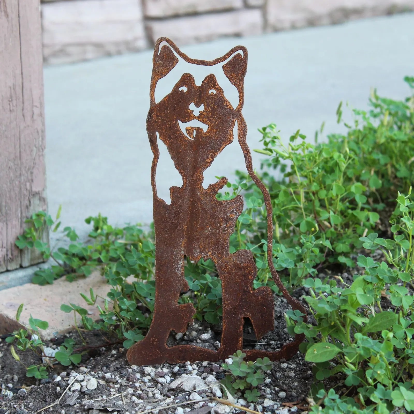 Rusty Corten steel silhouette of a sitting Siberian Husky surrounded by green foliage, perfect for outdoor dog decor.