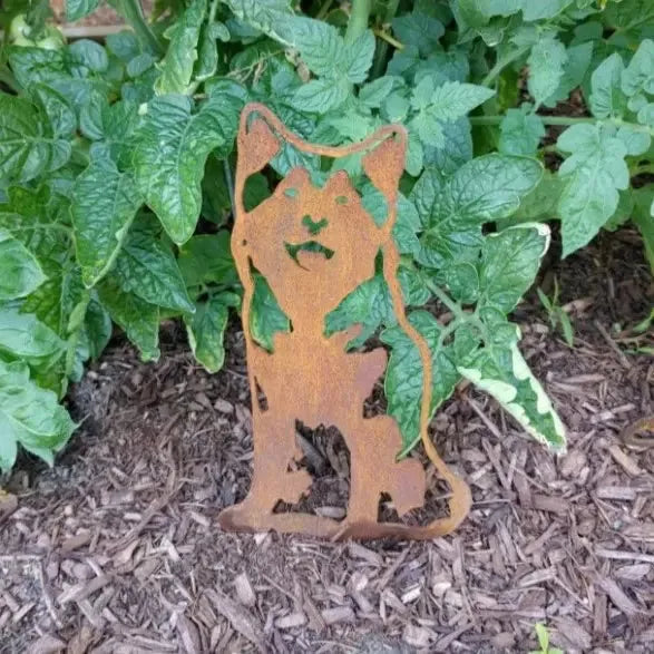 Rusty Corten steel silhouette of a Siberian Husky nestled among green leaves and mulch in an outdoor setting.