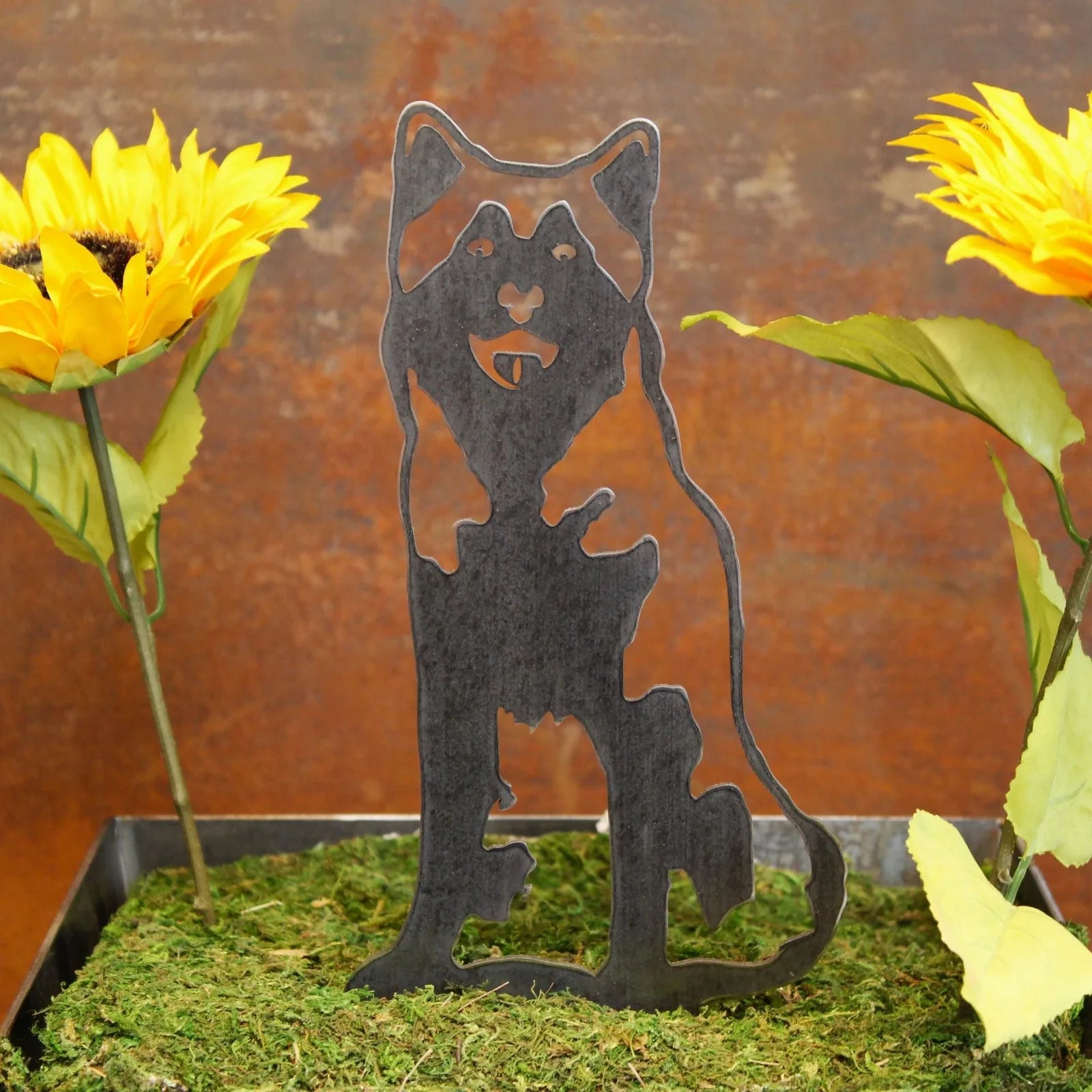 Siberian Husky metal silhouette in matte black, placed among sunflowers on mossy ground, perfect for outdoor dog decor.
