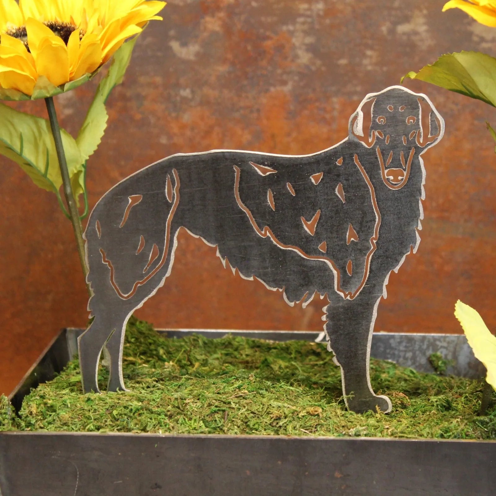 Silken Windhound metal silhouette in matte black, showcased in a decorative planter with greenery and sunflowers.