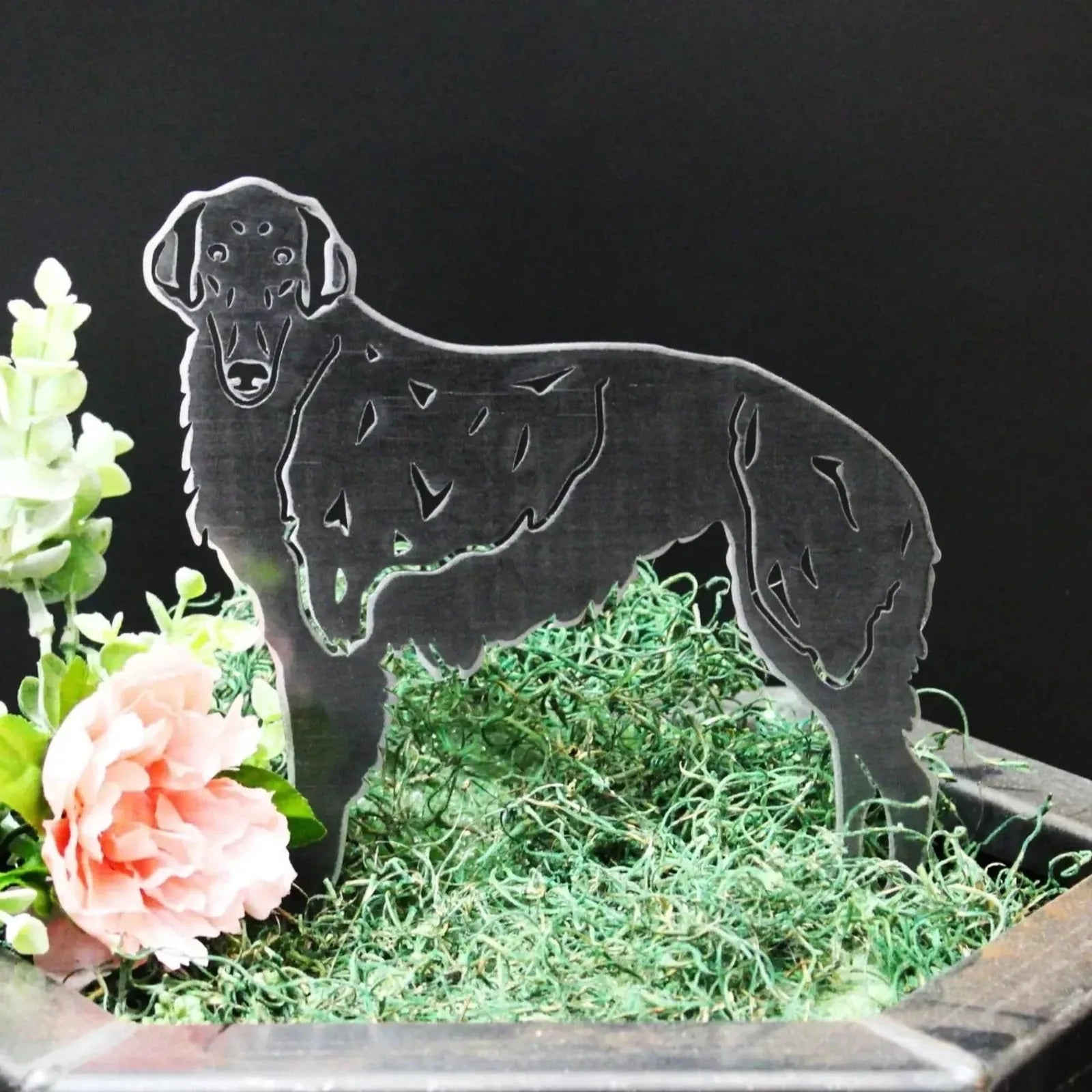 Silken Windhound metal silhouette in black, resting on green moss and surrounded by floral decor.