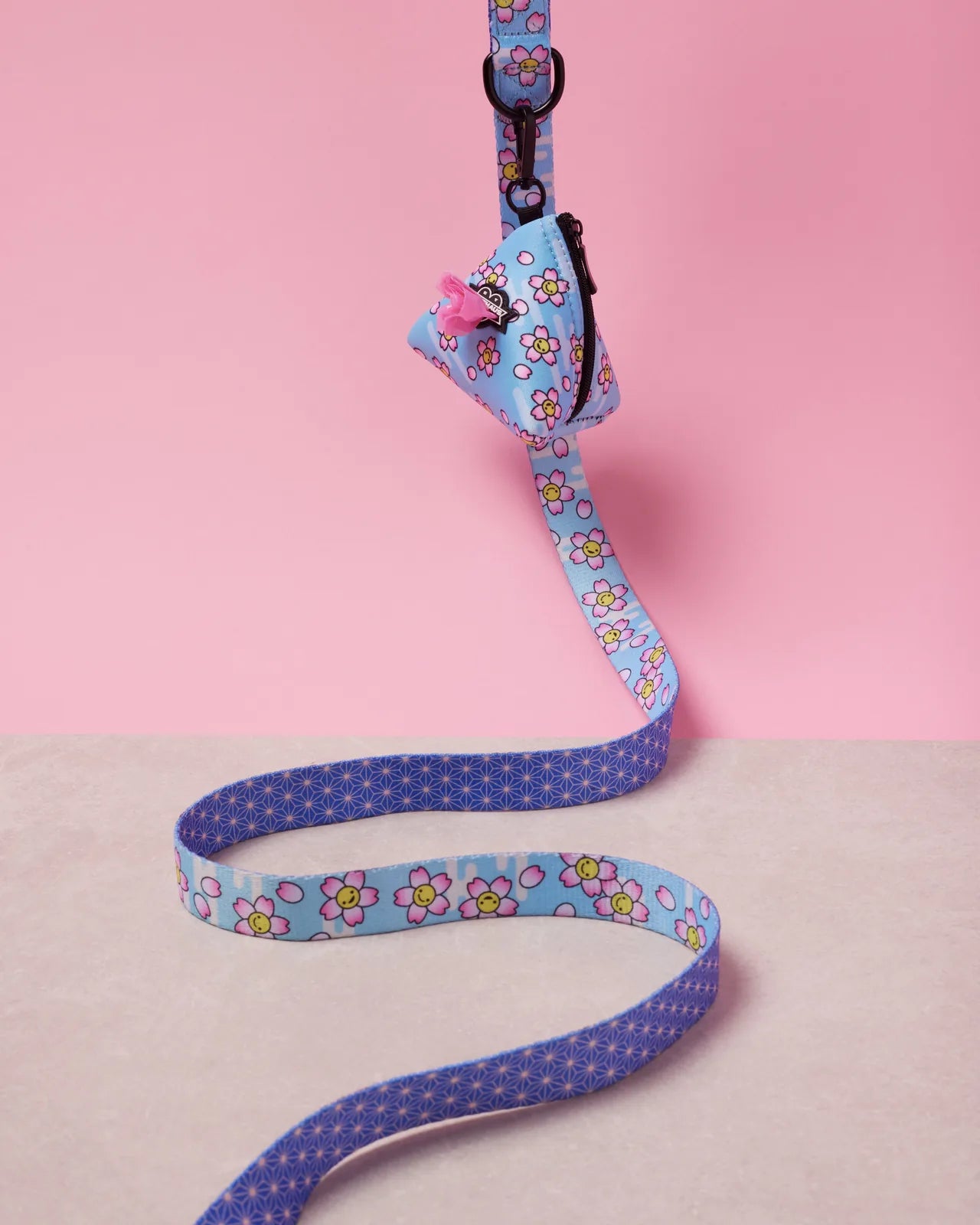 Blue floral-patterned dog poop bag holder attached to a leash, set against a pink background.