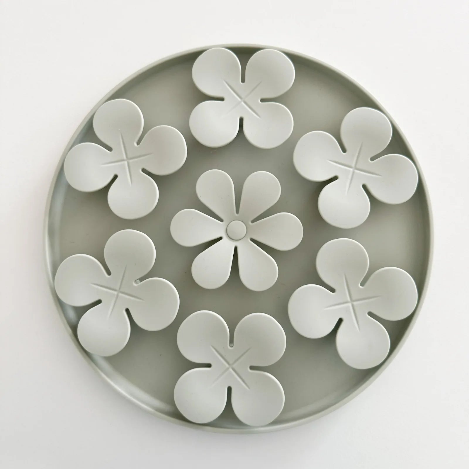 Light gray circular snuffle mat with flower-shaped compartments, designed for hiding dog treats.