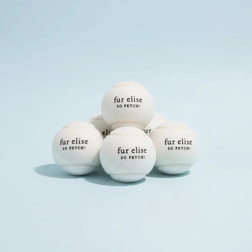 Ivory tennis balls with "fur elise SO FETCH!" text, featuring a soft felt surface and durable design, stacked together.