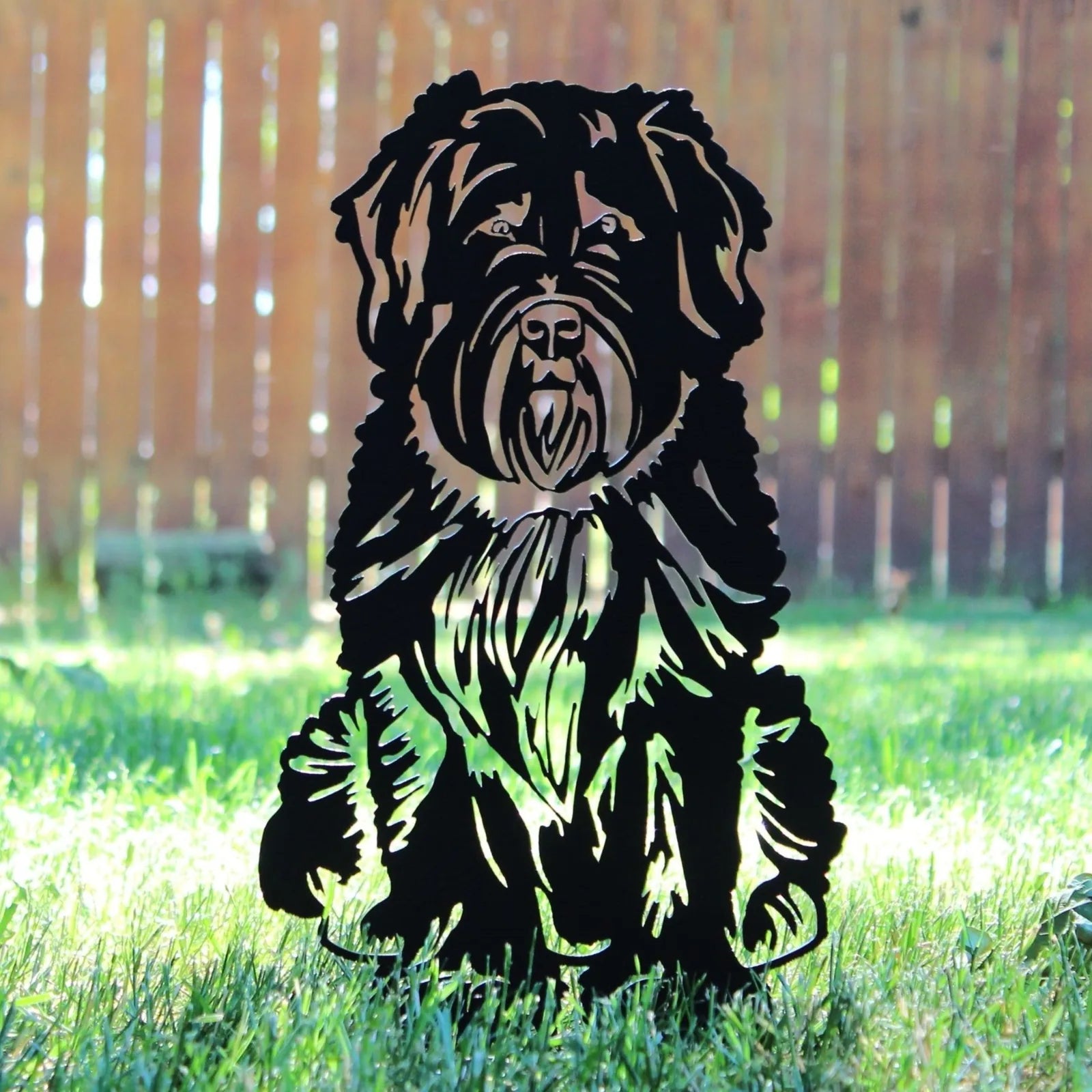 Soft Coated Wheaten Terrier metal silhouette in black, displayed in grass against a wooden fence background.