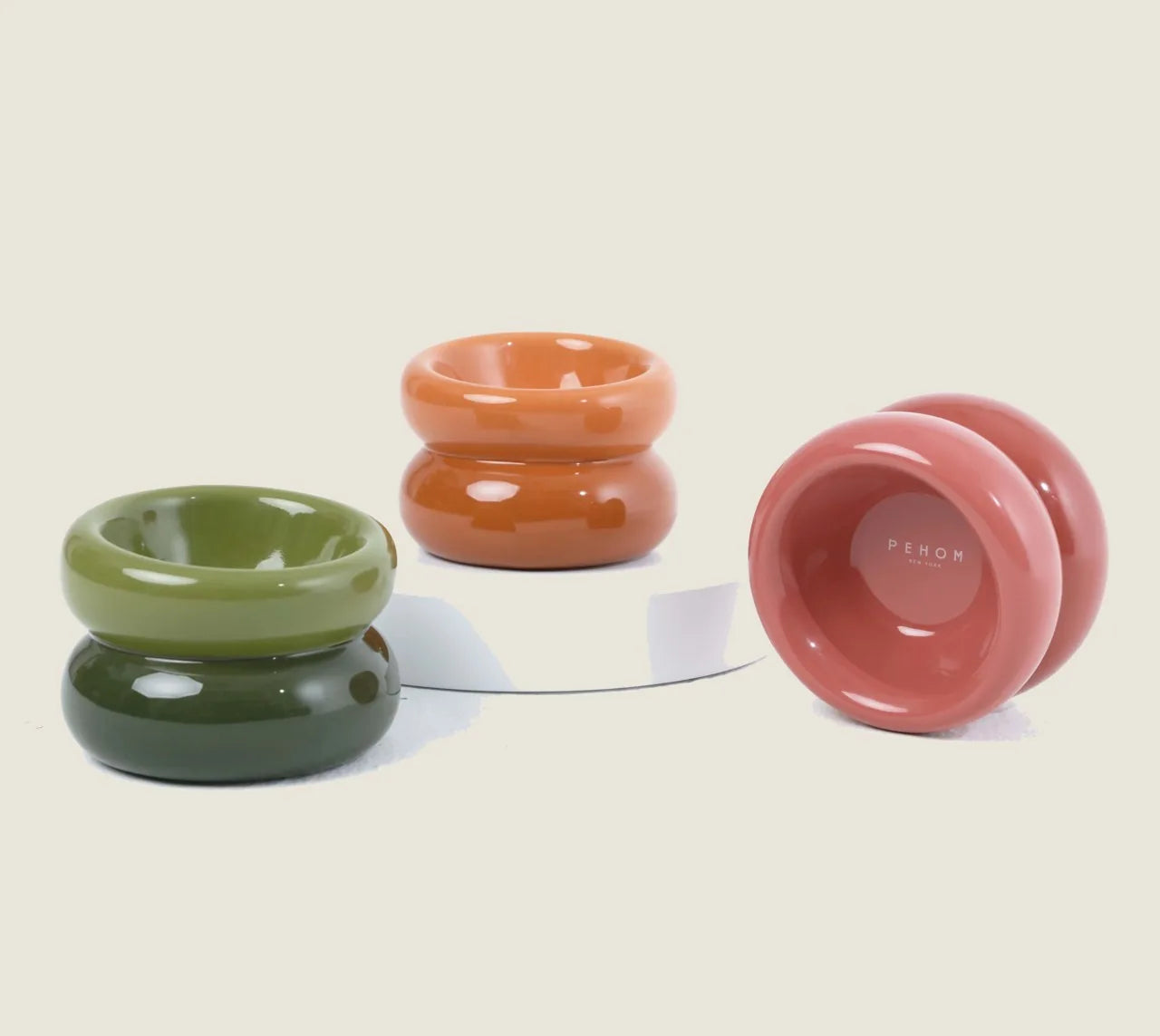 Amber orange soufflé pet bowl with smooth design, paired with green and pink bowls on a white surface.