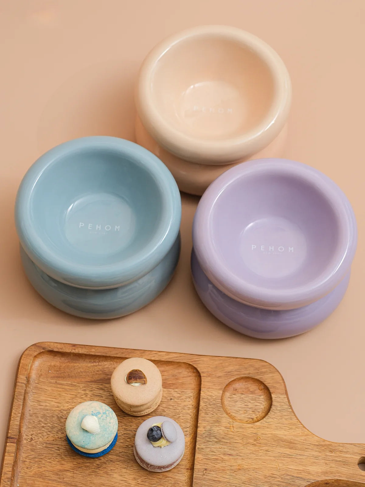 Cream beige pet bowl with a smooth finish, alongside blue and lavender bowls on a wooden tray. Designed for easy feeding.