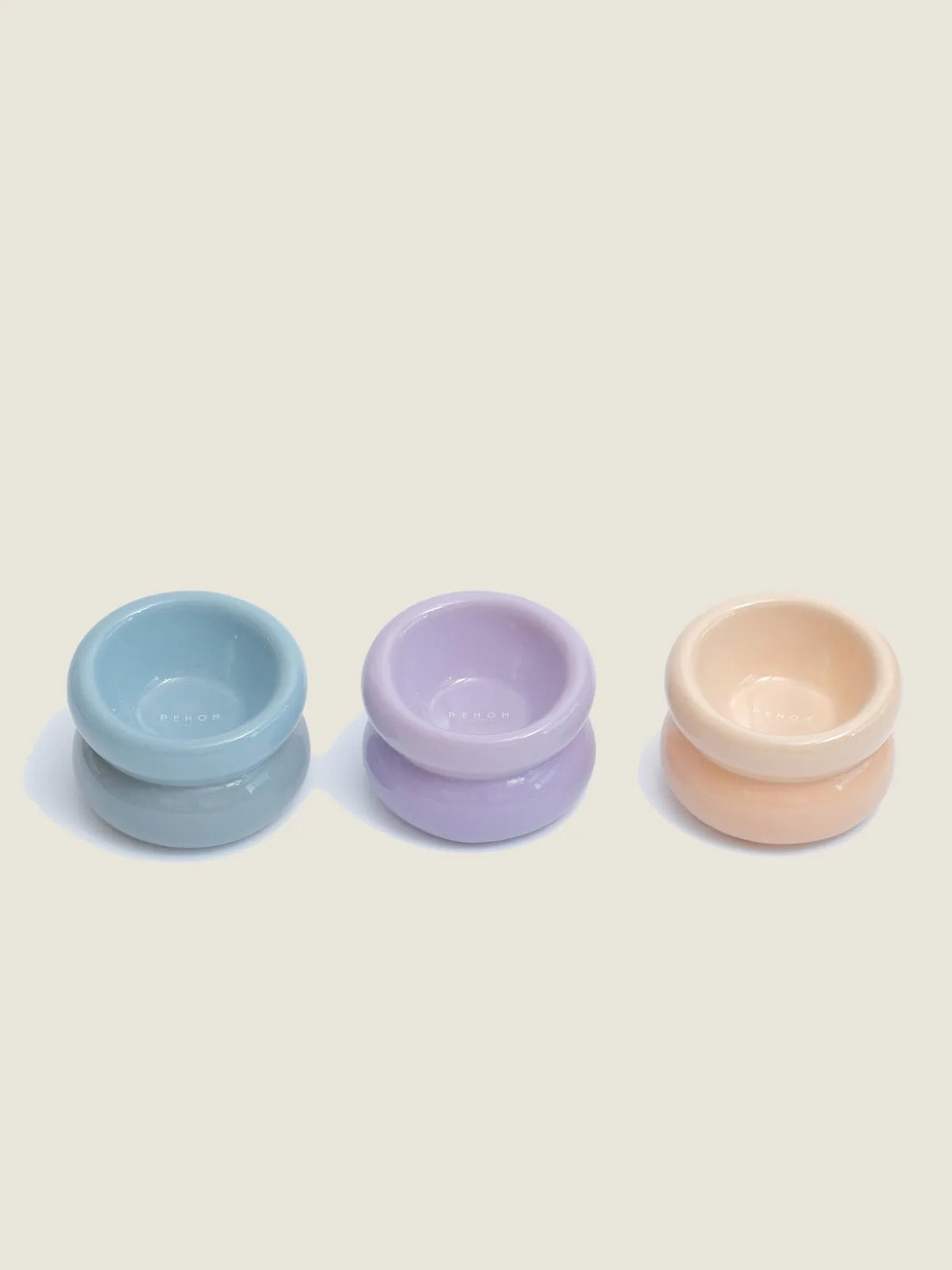 Cream beige pet bowl with a diagonal opening, smooth finish, and stable wide base, part of a colorful set.