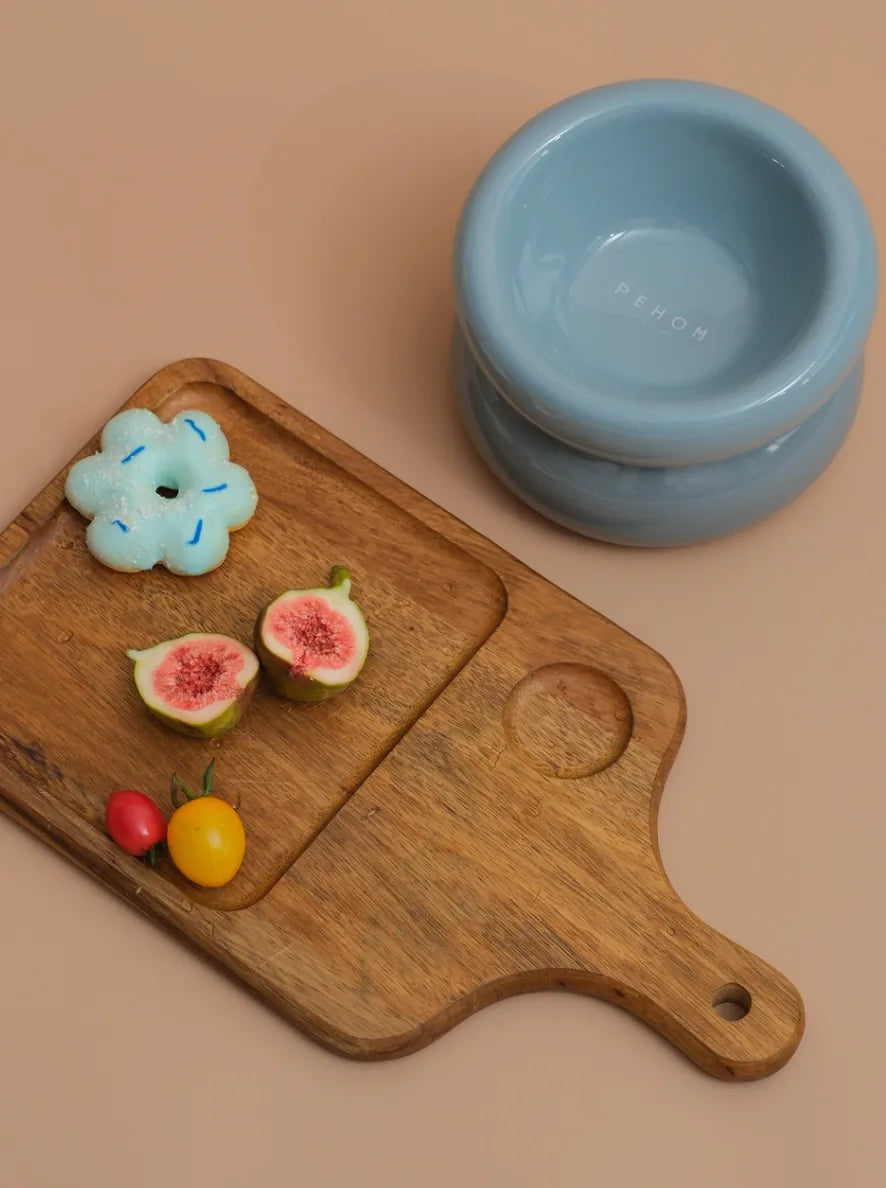 Soufflé Pet Bowl in Frozen Blue beside a wooden tray with sliced figs and colorful fruit.